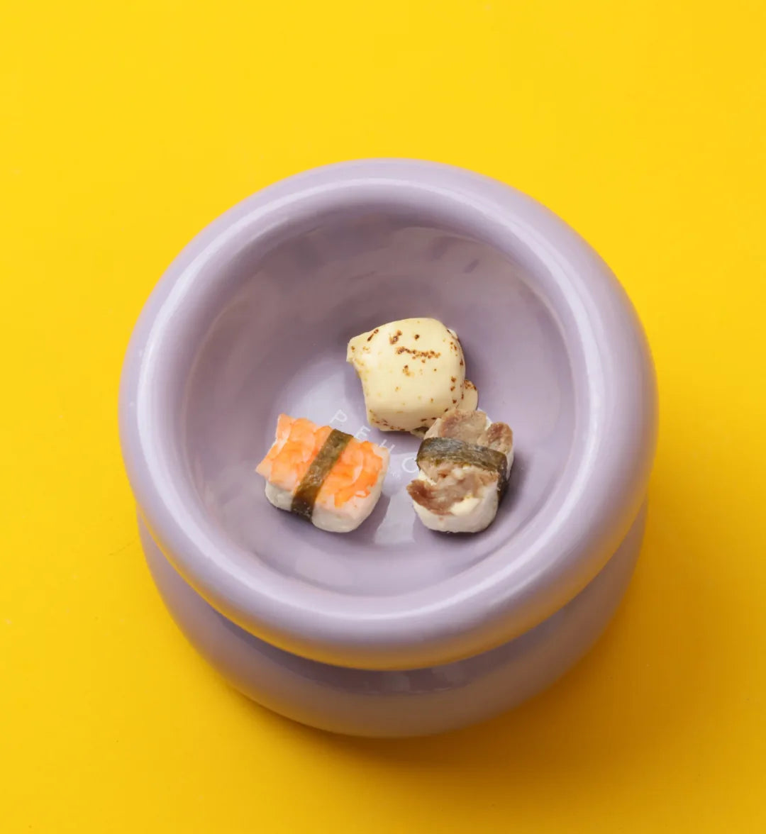 Purple soufflé pet bowl featuring a diagonal opening and small toy sushi inside, set against a bright yellow background.