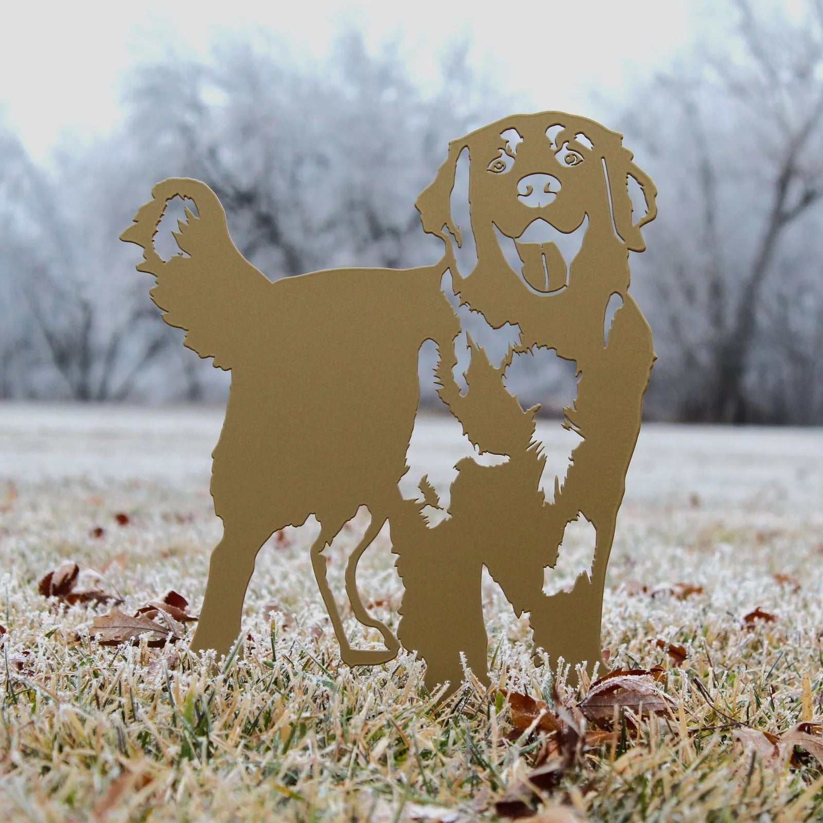 Standing silhouette of a golden retriever in metallic gold, set on frosty grass among fallen leaves.