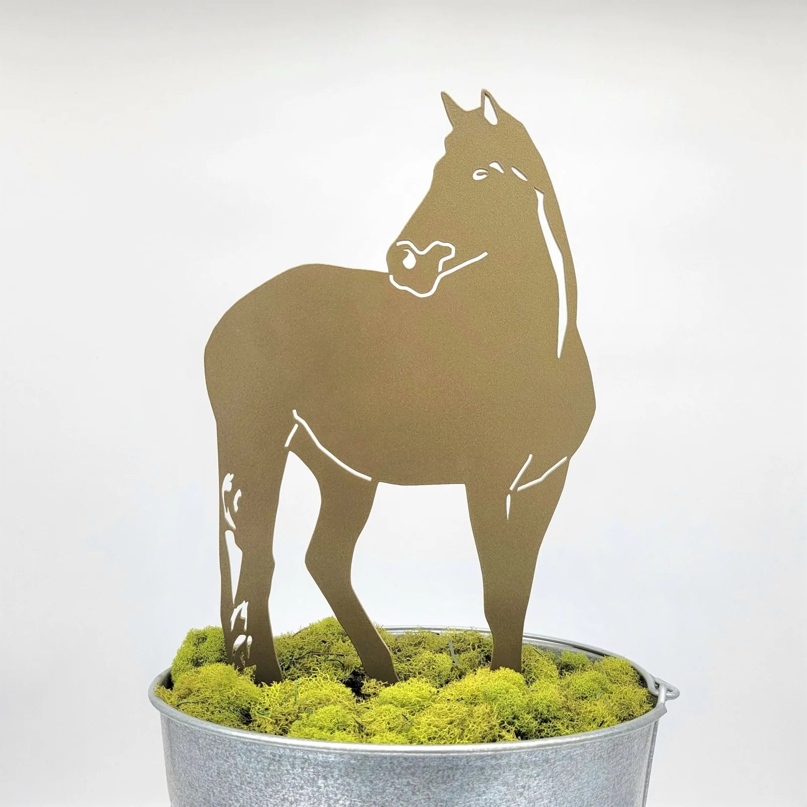 Gold metal horse silhouette standing in a galvanized pot filled with green moss, showcasing outdoor decor artistry.