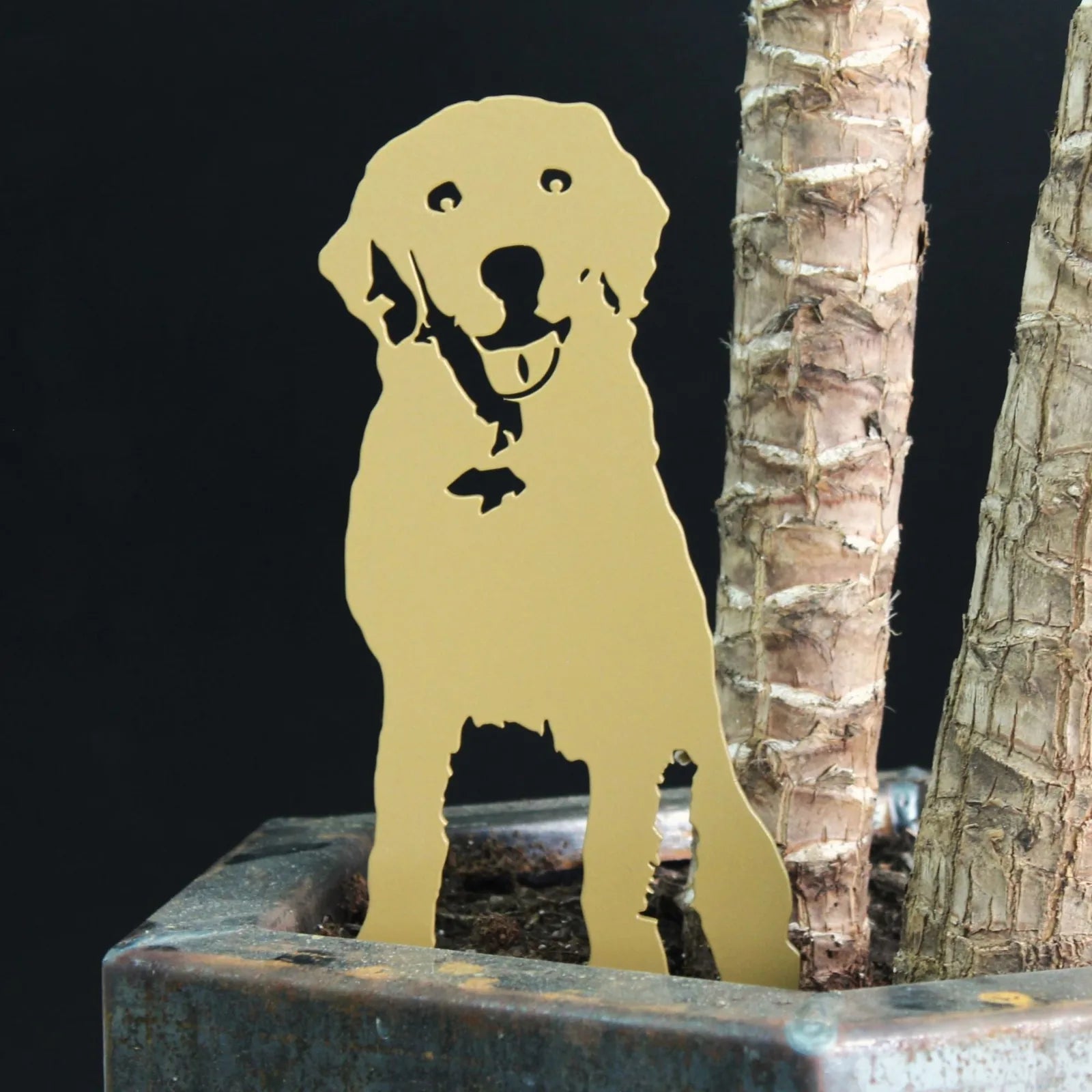 Metal silhouette of a smiling Labrador Retriever in metallic gold, positioned among plant roots in a decorative pot.