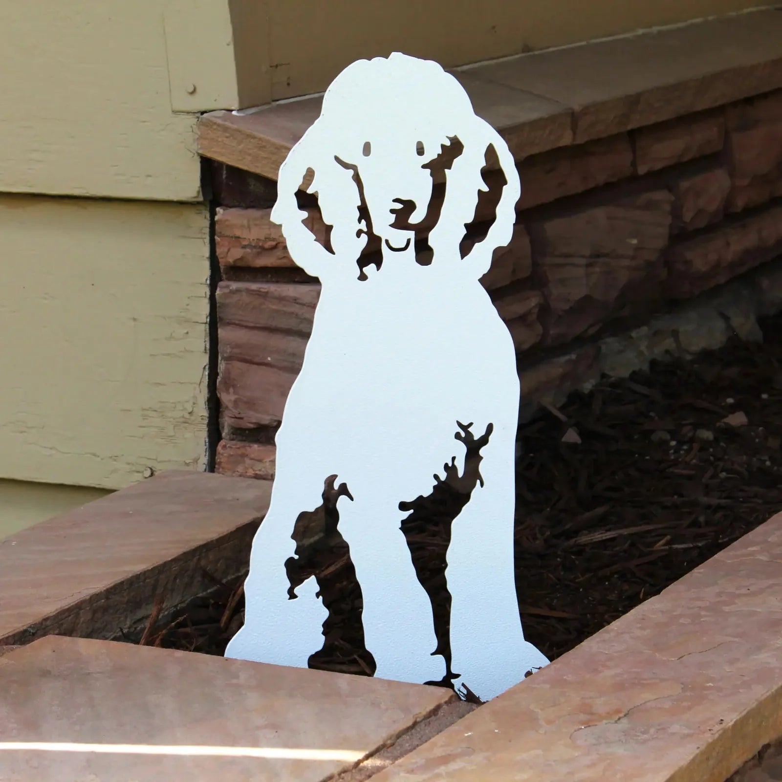 Glossy white metal silhouette of a poodle sits beside stones, showcasing intricate cutout details for outdoor decor.