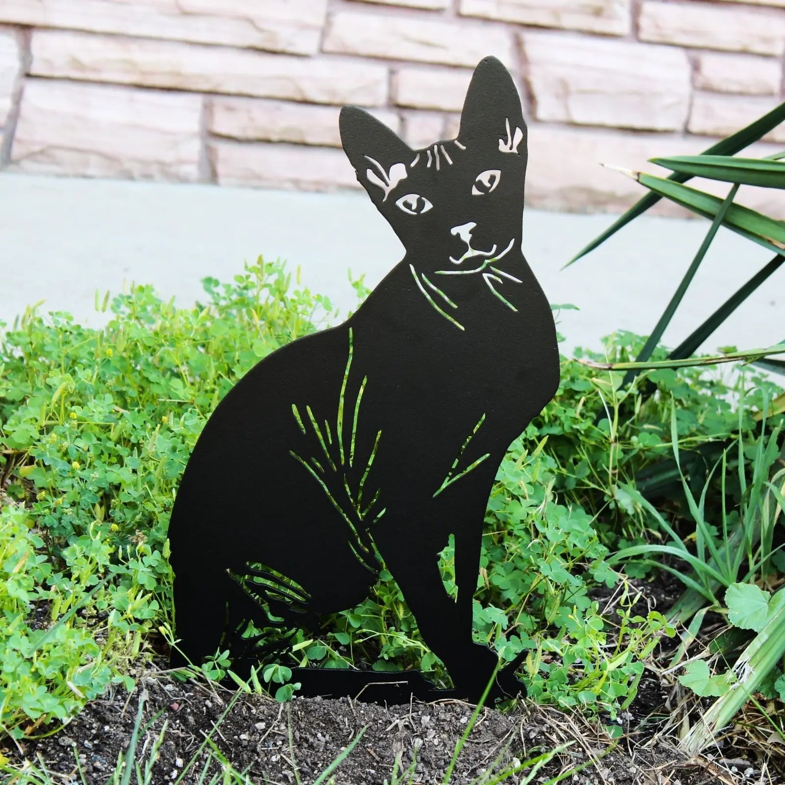 Handmade black metal Sphynx silhouette garden art surrounded by lush greenery, showcasing detailed cutouts and design.