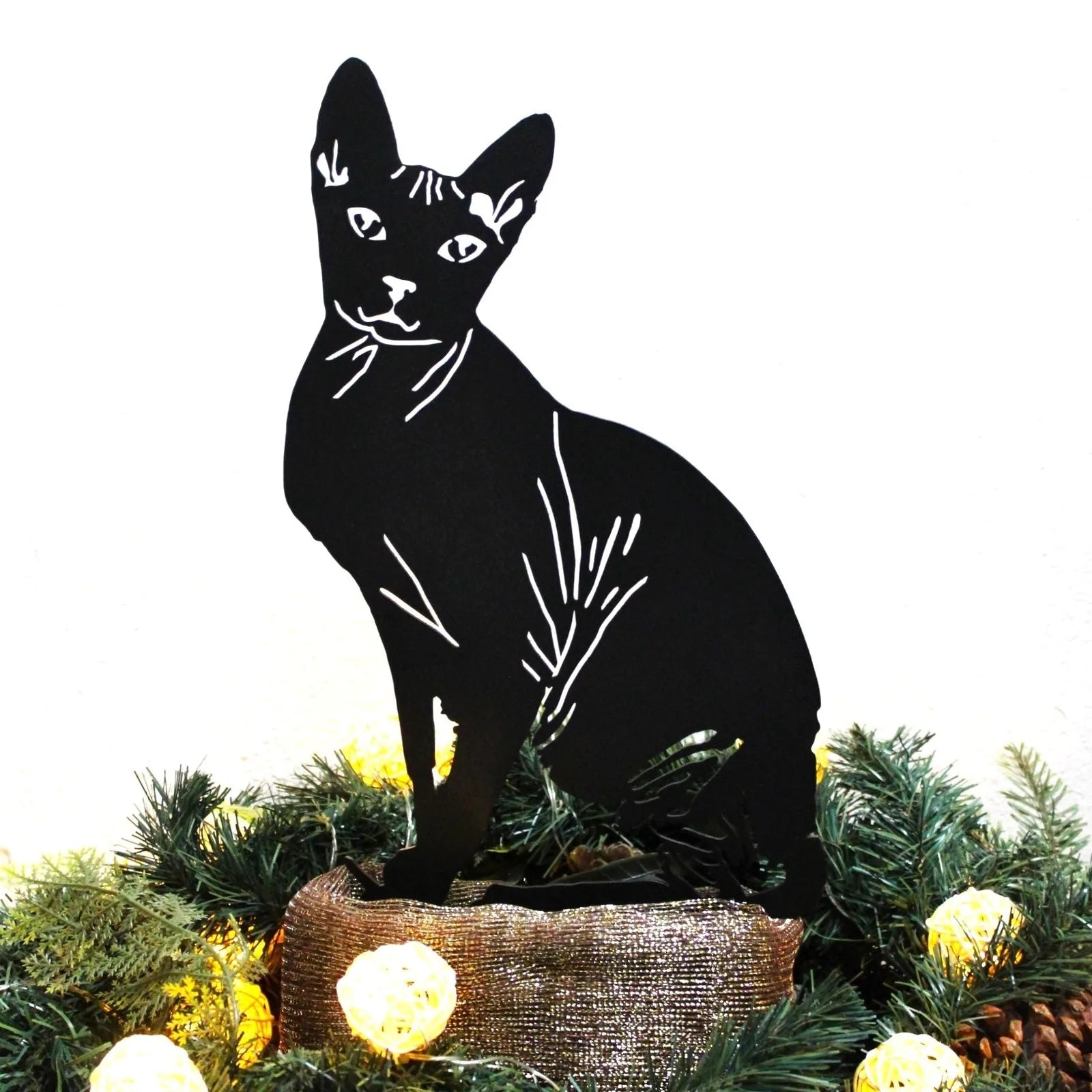 Black Sphynx silhouette garden art resting on greenery, with soft glowing lights in the background.