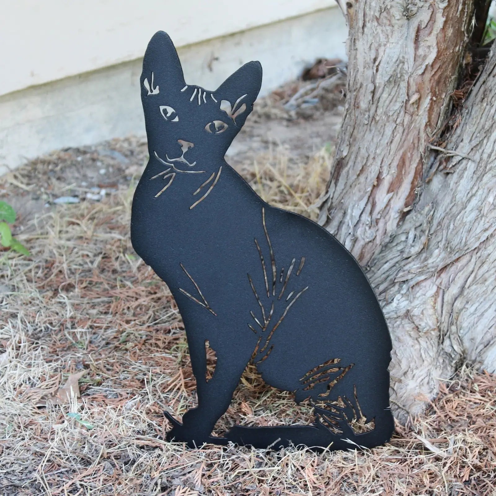 Black metal Sphynx cat silhouette garden art featuring cut-out details, positioned against a natural backdrop.