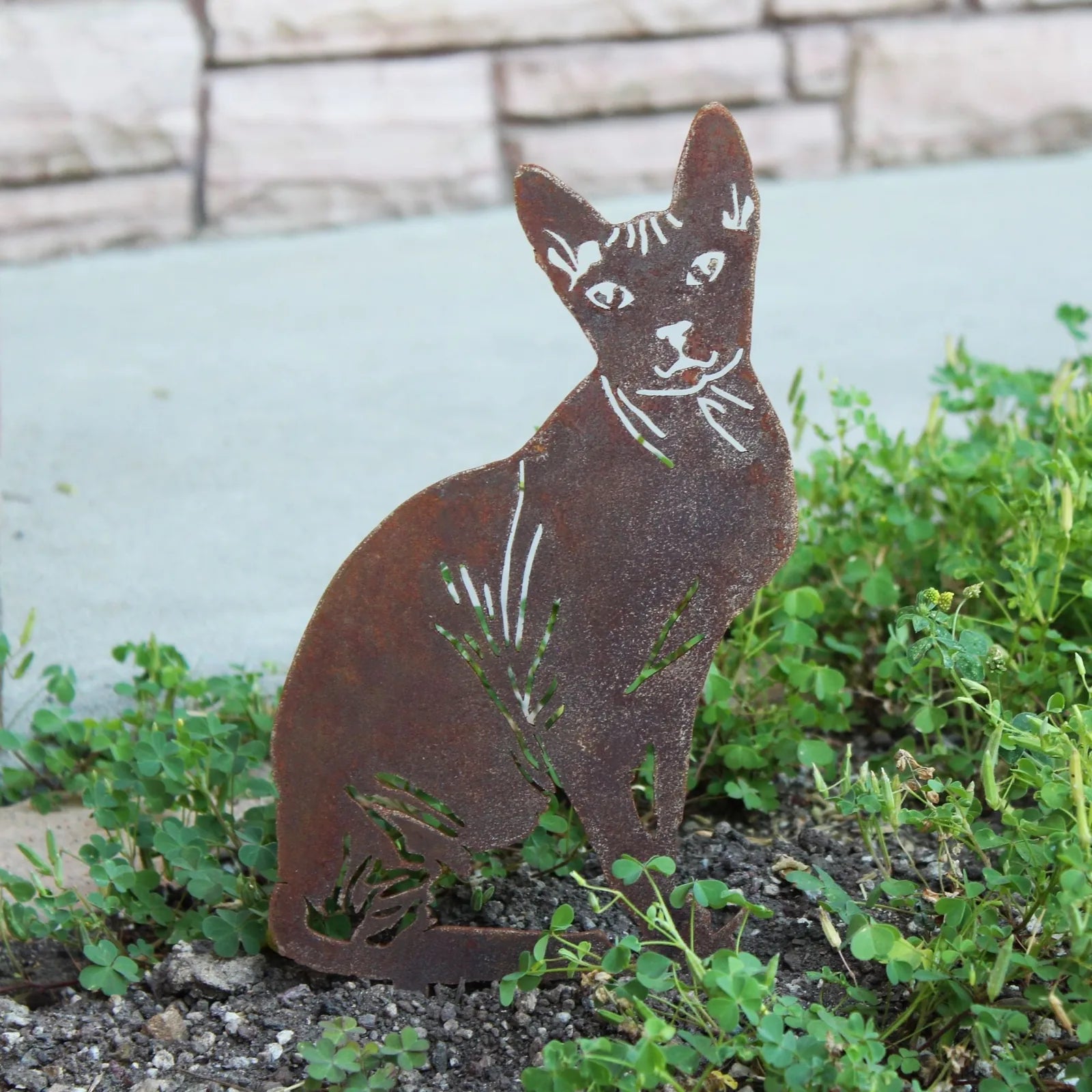 Rusty Corten steel Sphynx silhouette garden art among green plants, designed for outdoor display.