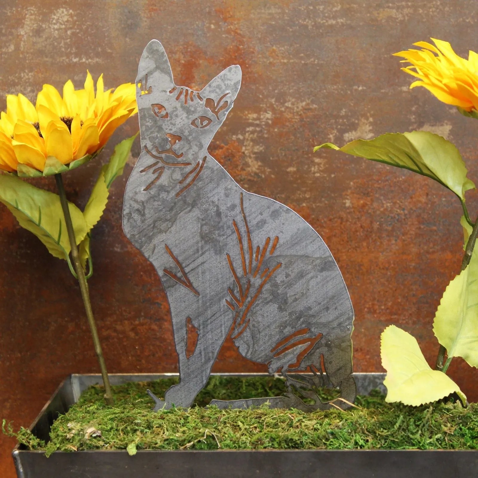 Handmade Sphynx silhouette in Corten steel, surrounded by sunflowers and greenery, perfect for outdoor décor.
