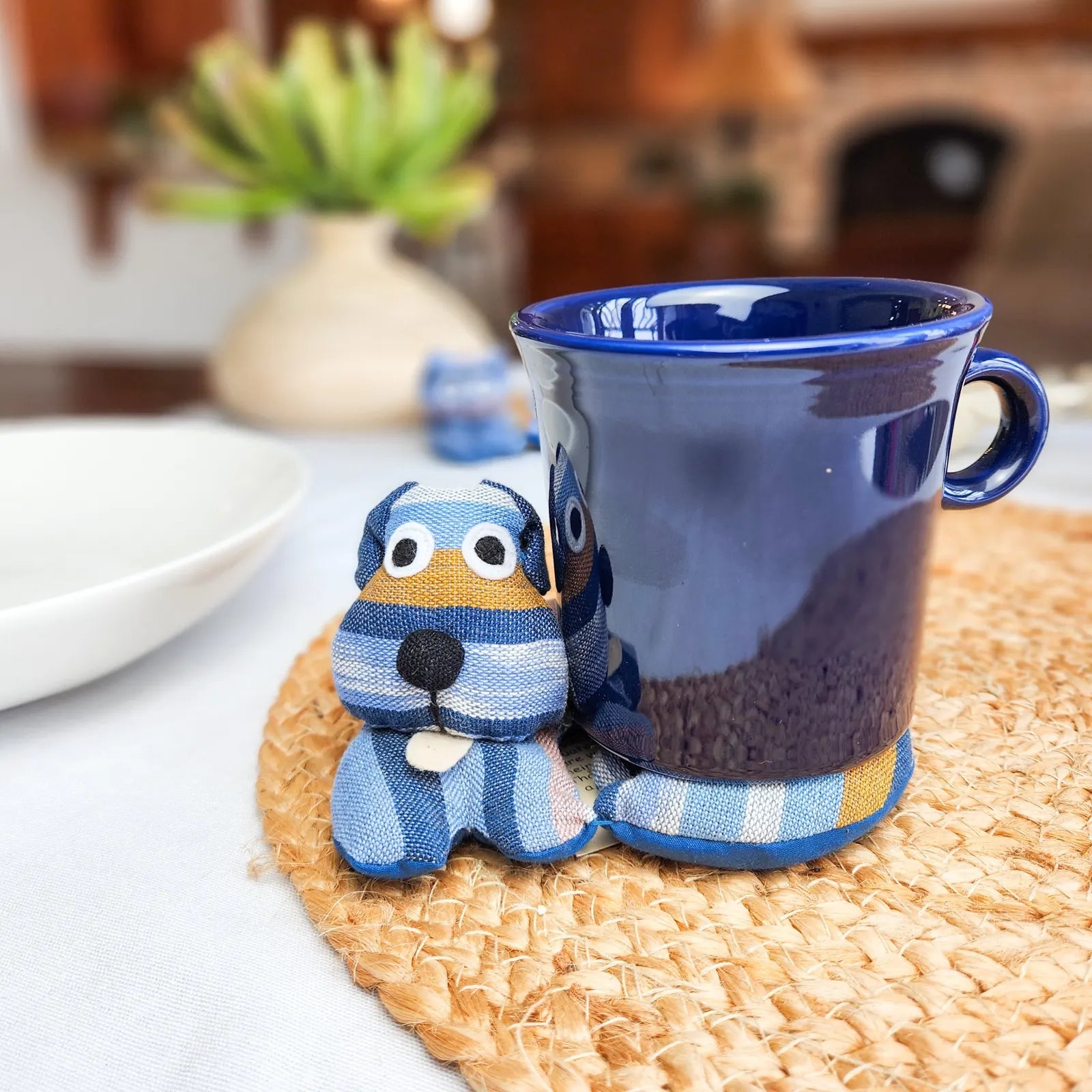 Handmade blue striped dog trivet next to a navy mug on a woven placemat, adding charm to the kitchen.