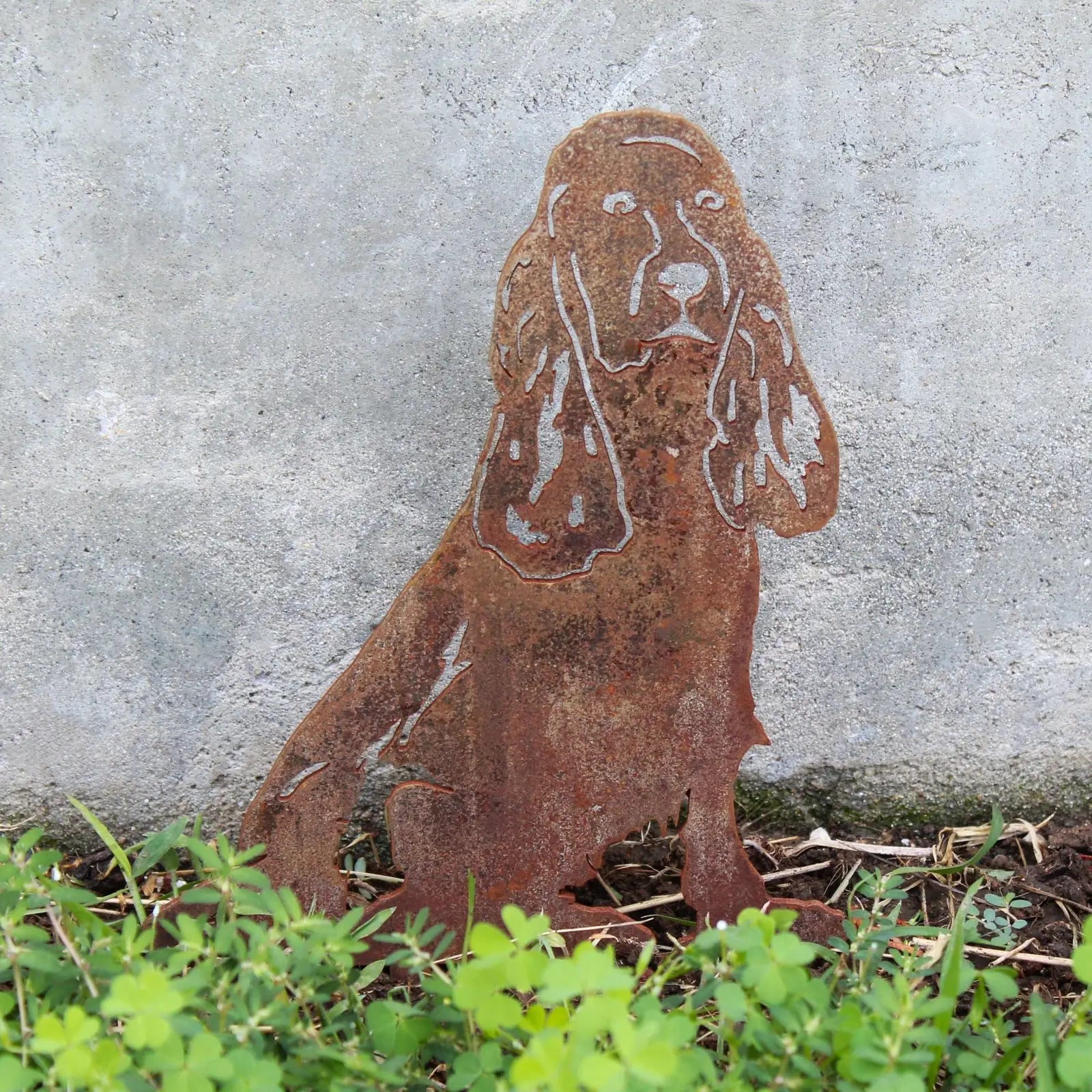 Rusty Corten steel silhouette of a Springer Spaniel, set against a concrete wall with greenery in the foreground.