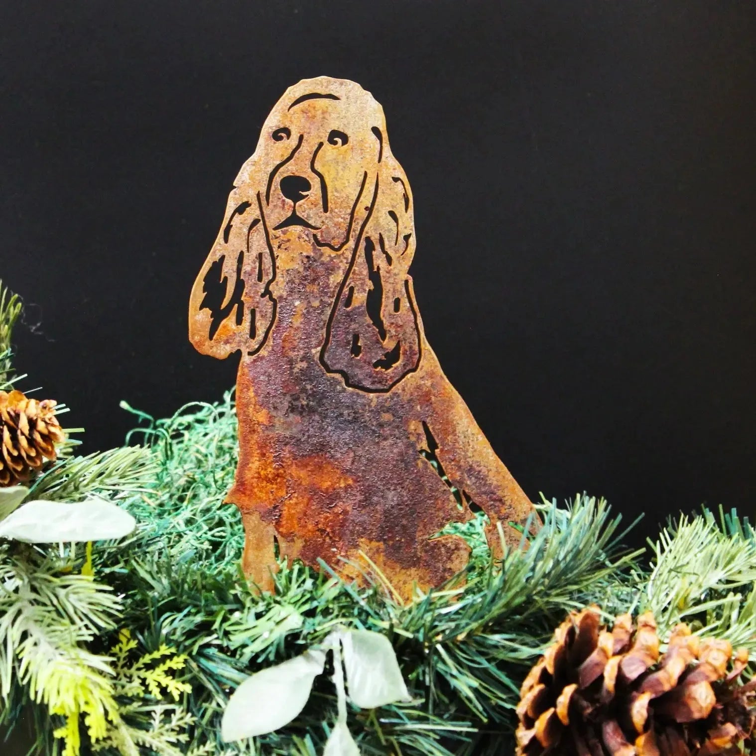 Rusty metal silhouette of a Springer Spaniel, surrounded by green foliage and pine cones, adding rustic outdoor charm.