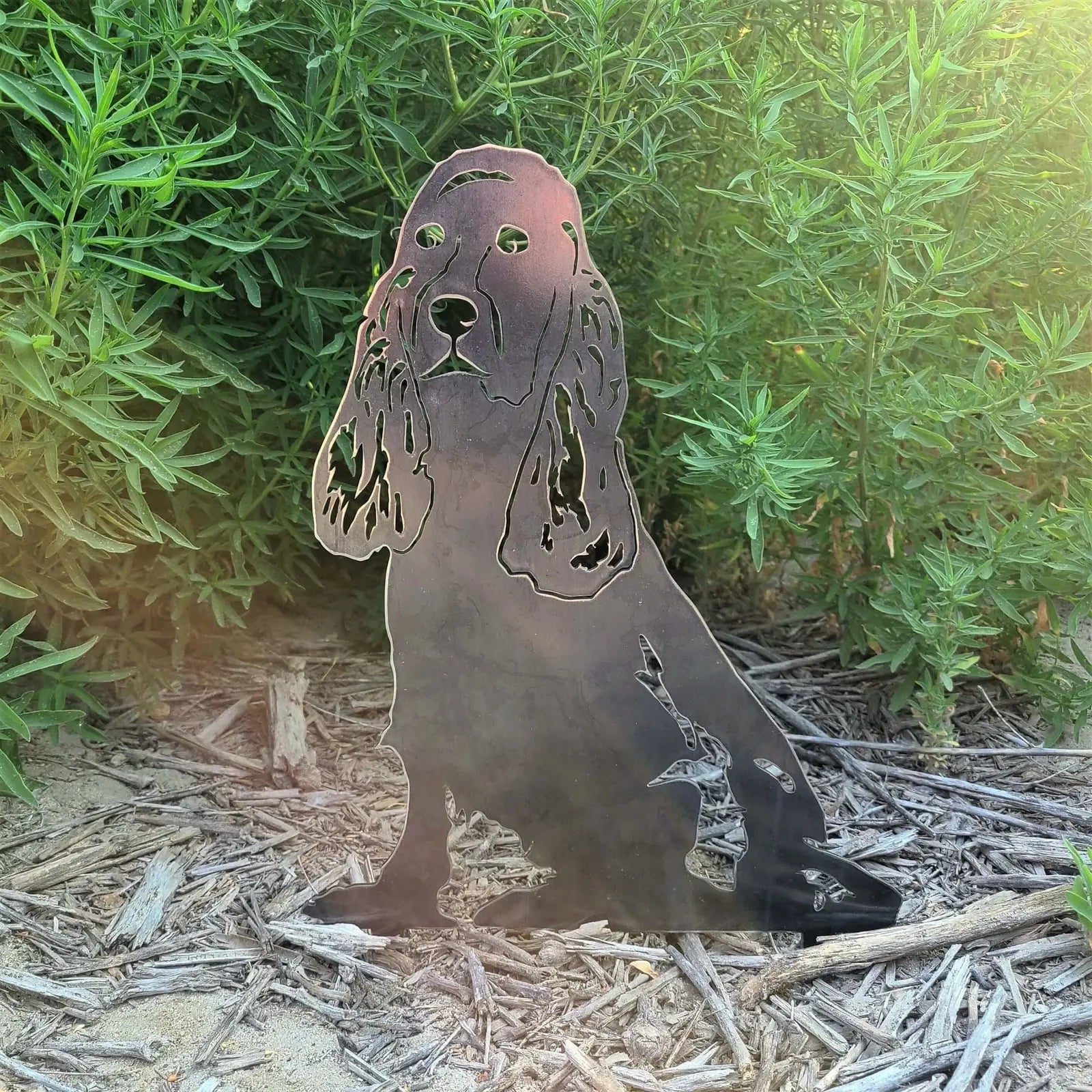 Springer Spaniel metal silhouette in weathered black Corten steel, surrounded by greenery and mulch.