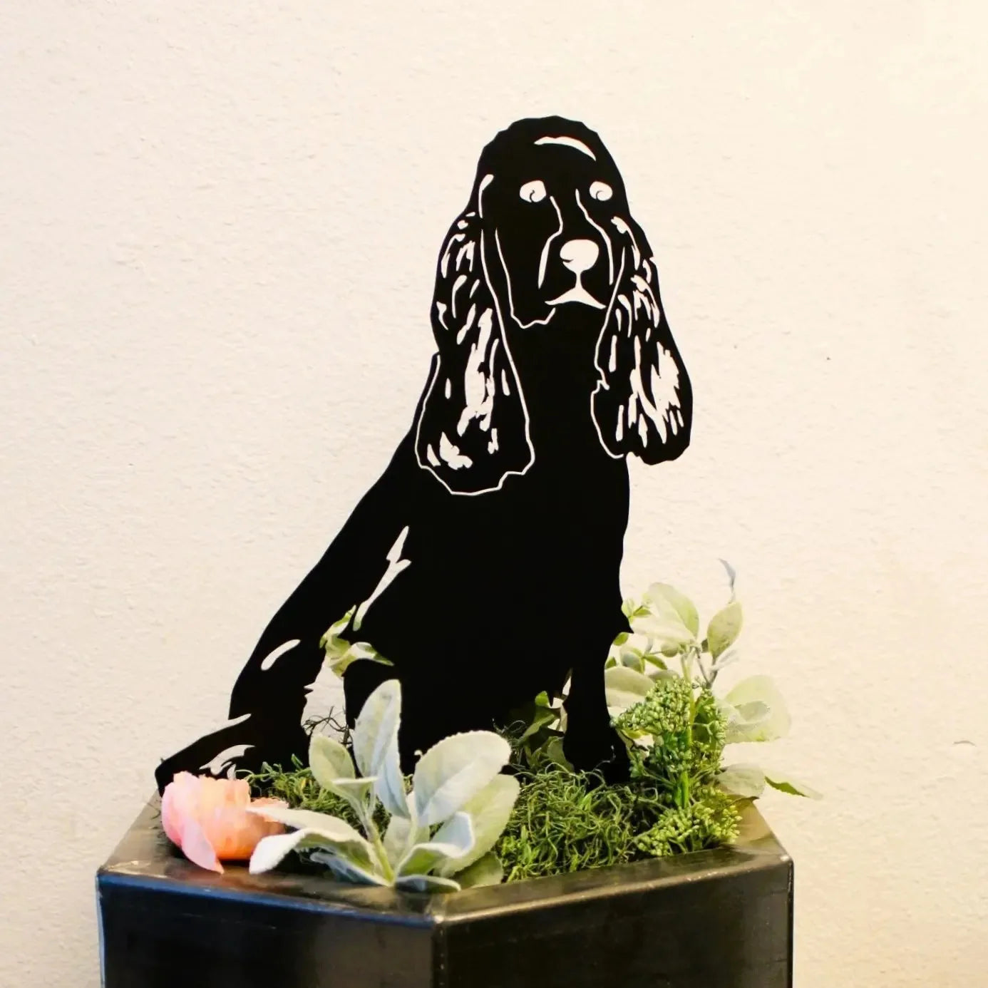 Black metal silhouette of a Springer Spaniel sitting in greenery, showcasing detailed features and rustic charm.