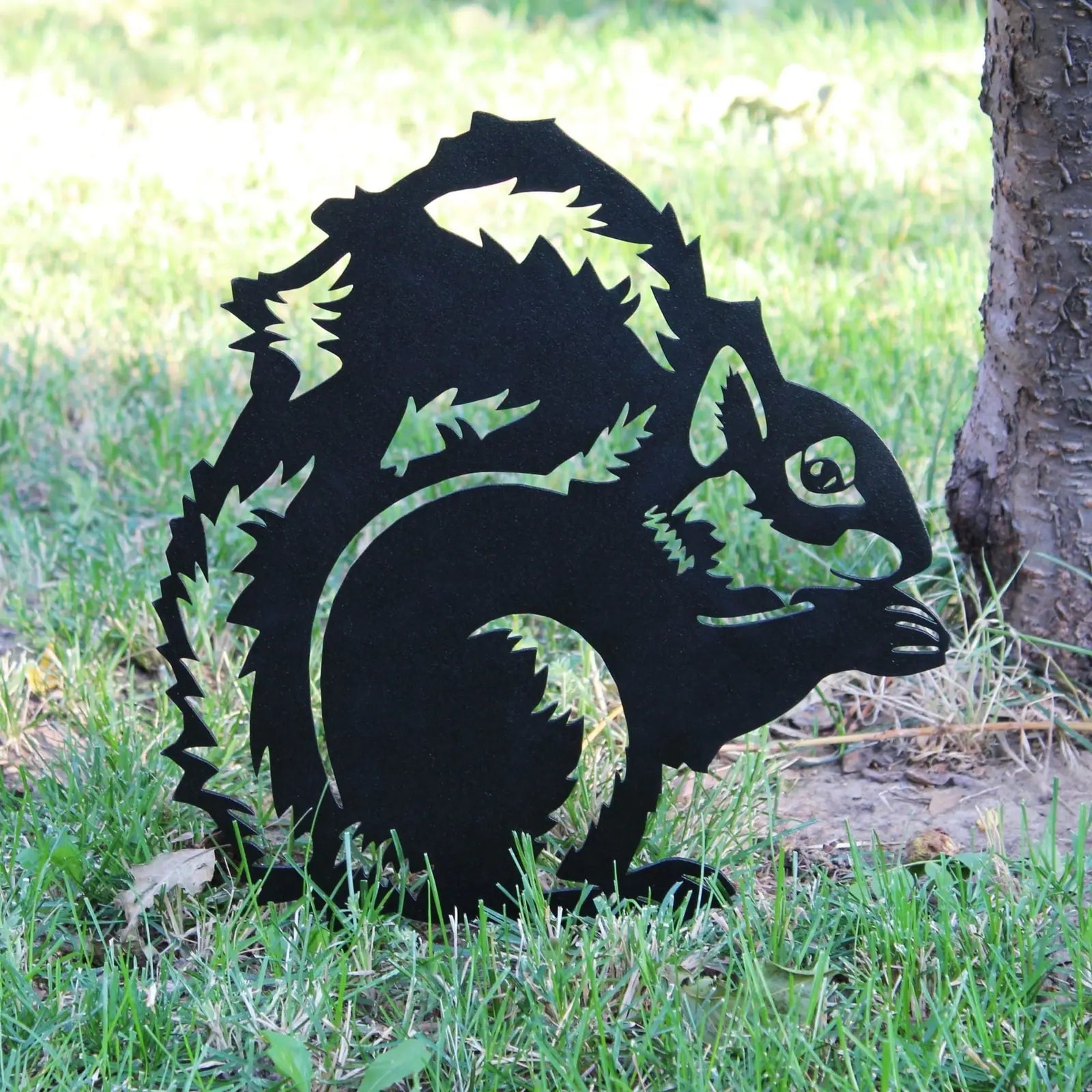 Black metal silhouette of a squirrel, detailed with cut-out leaves, set in grassy outdoor decor.
