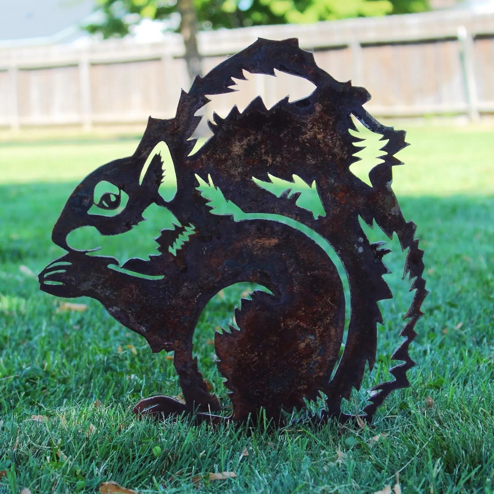 Handmade rusted Corten steel squirrel silhouette, featuring detailed cutouts, against green grass background.