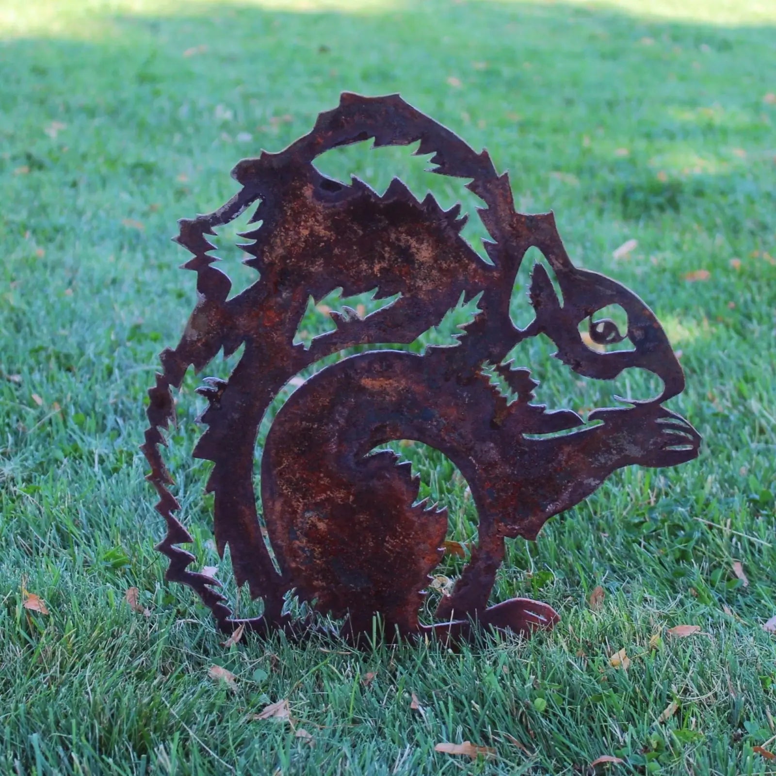 Corten steel squirrel silhouette with rust patina, set on green grass, showcasing detailed metal art design.
