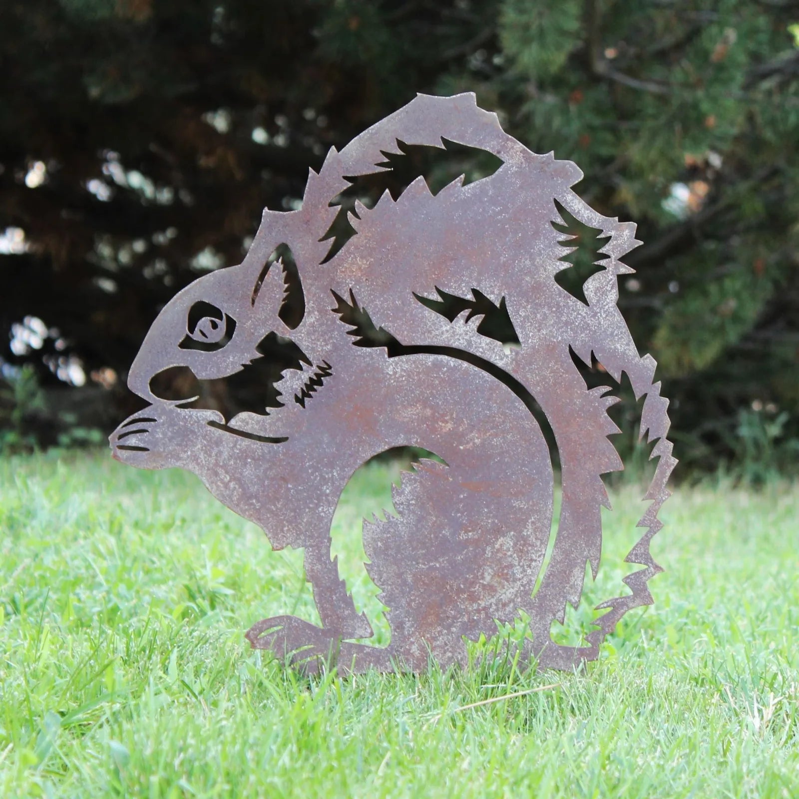 Handmade rusted metal silhouette of a squirrel, featuring intricate details, set against green grass background.