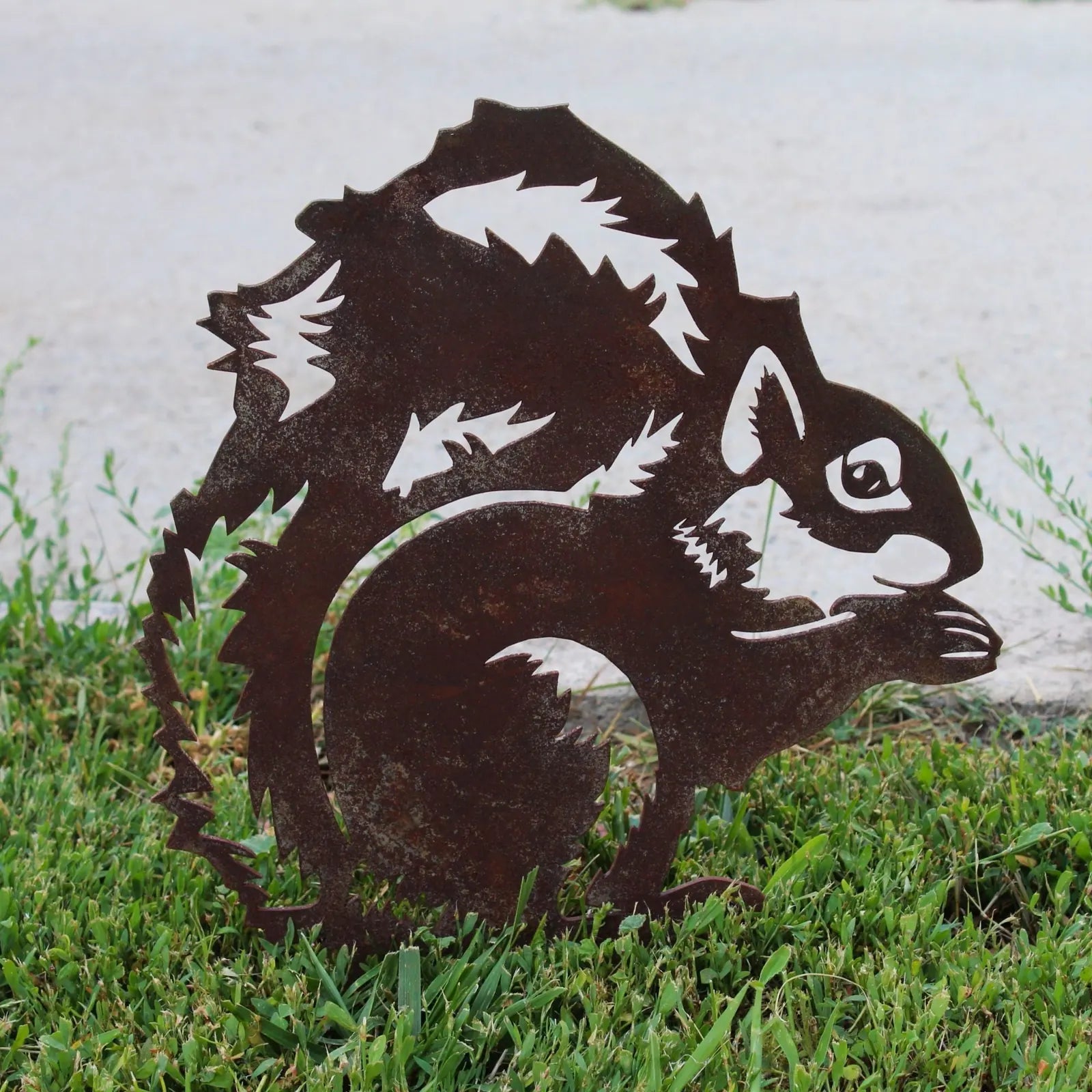 Rustic Corten steel silhouette of a squirrel, detailed with leaves, set in green grass for outdoor garden decor.