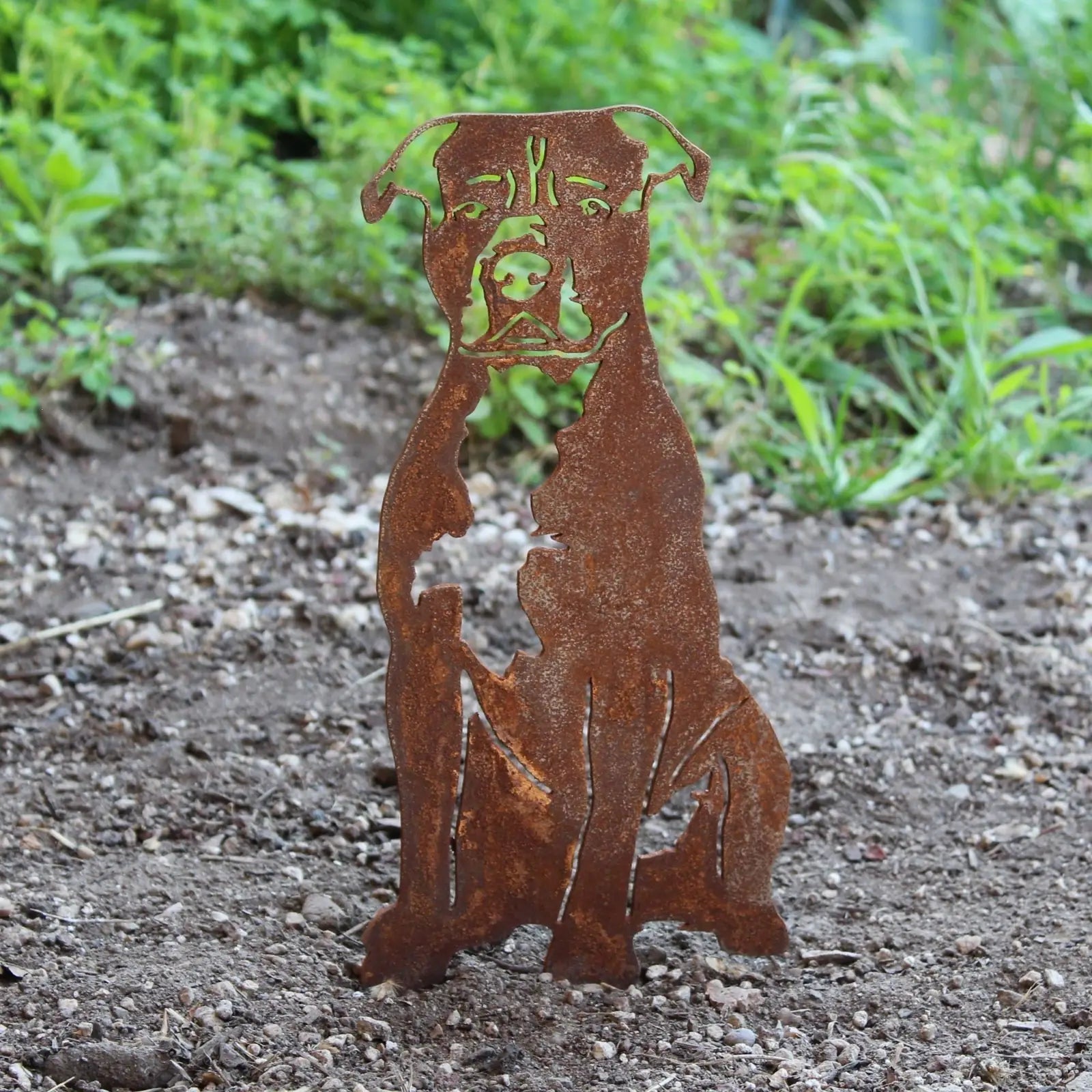 Rusty metal silhouette of a Staffordshire Bull Terrier seated in a garden, designed for outdoor decor.