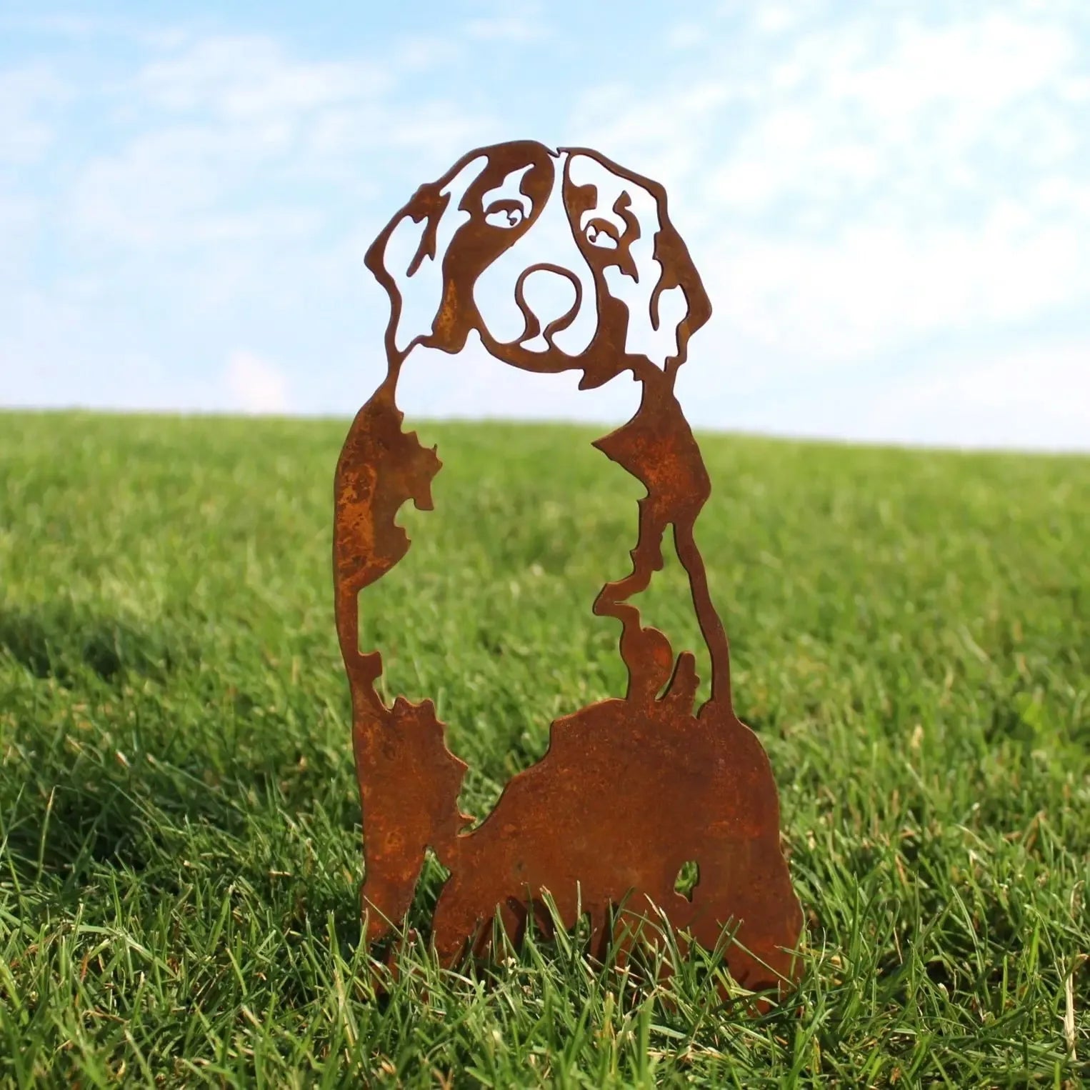 Rusty Corten steel silhouette of a Swiss Mountain Dog, standing amidst vibrant green grass under a blue sky.
