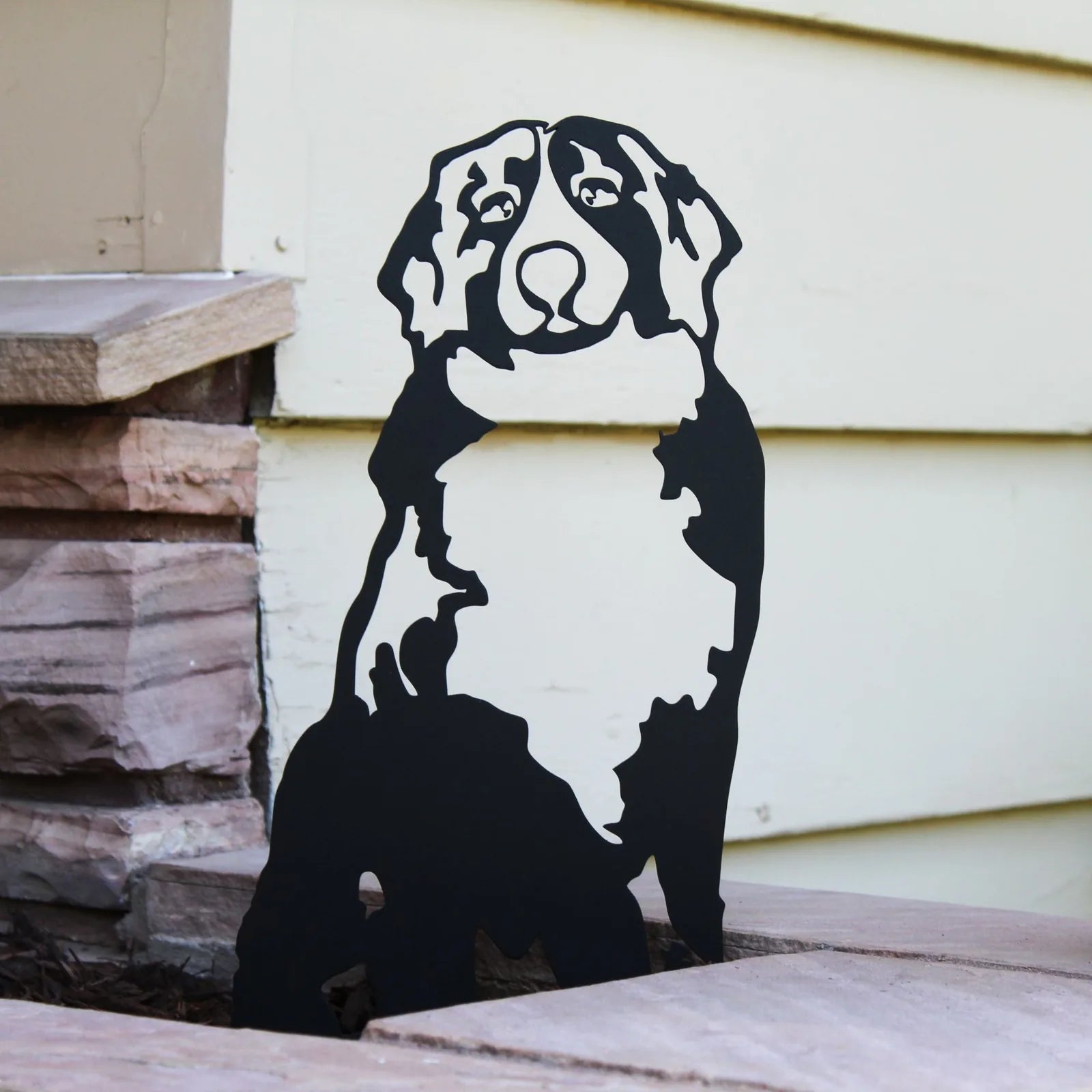 Black metal silhouette of a Swiss Mountain Dog standing on a stone surface against a pale backdrop.