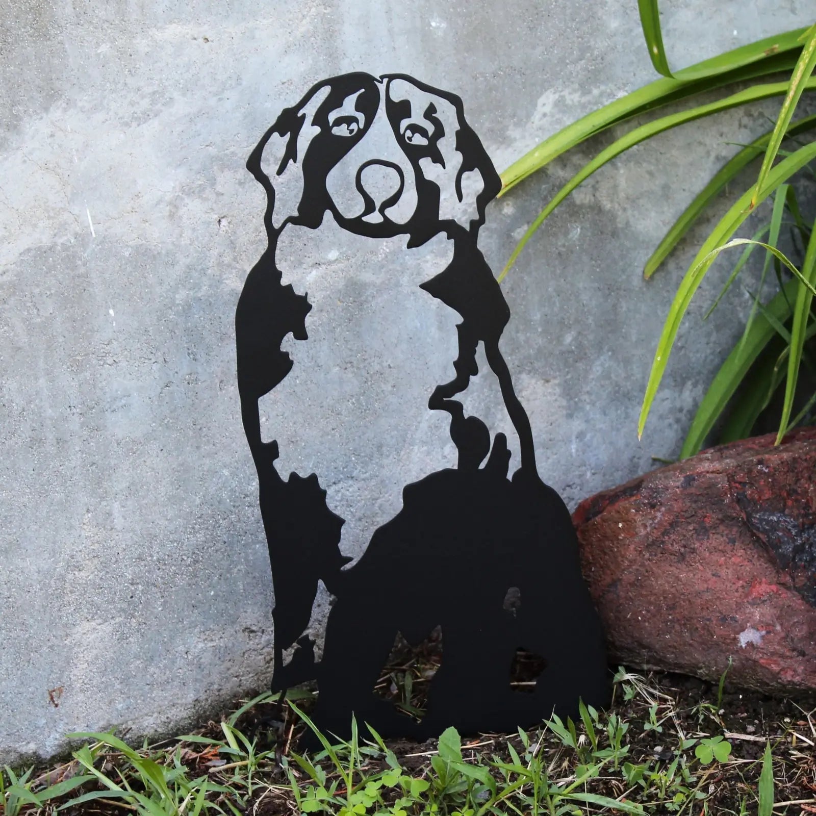 Black metal silhouette of a Swiss Mountain Dog surrounded by grass and stones, perfect for outdoor dog decor.