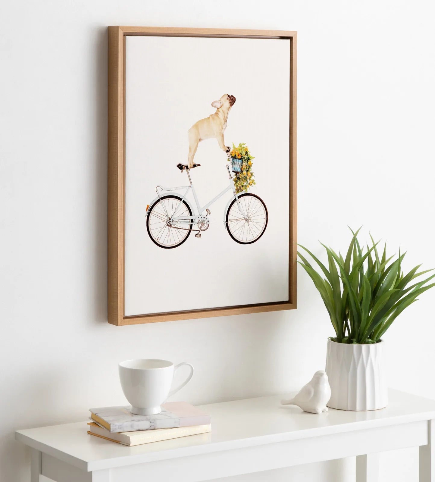 Framed canvas artwork of a French Bulldog balancing on a bicycle with a plant basket, featuring a natural wood frame.