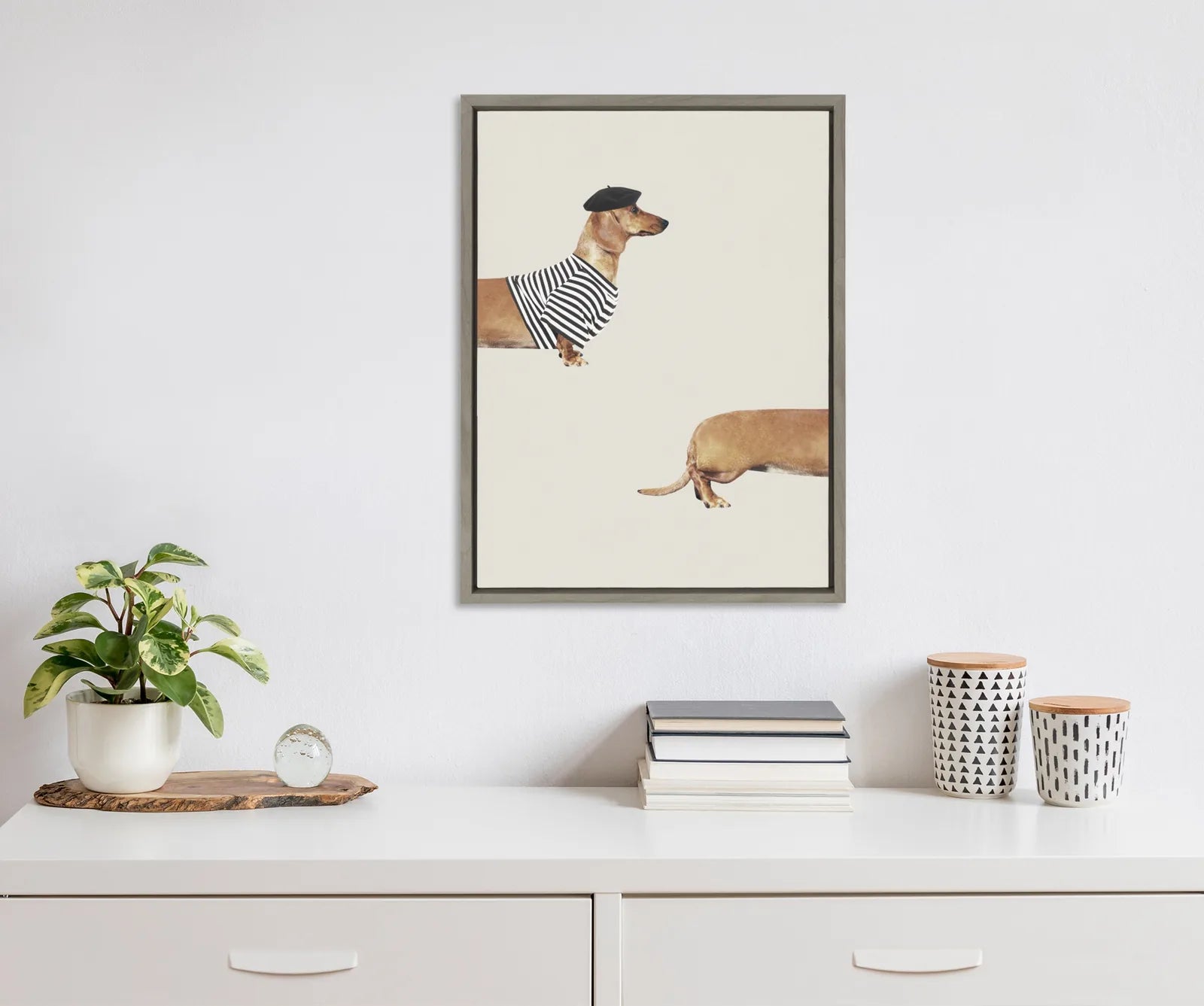 Framed canvas art featuring a long dog in a striped shirt and beret, displayed above a modern white shelf.