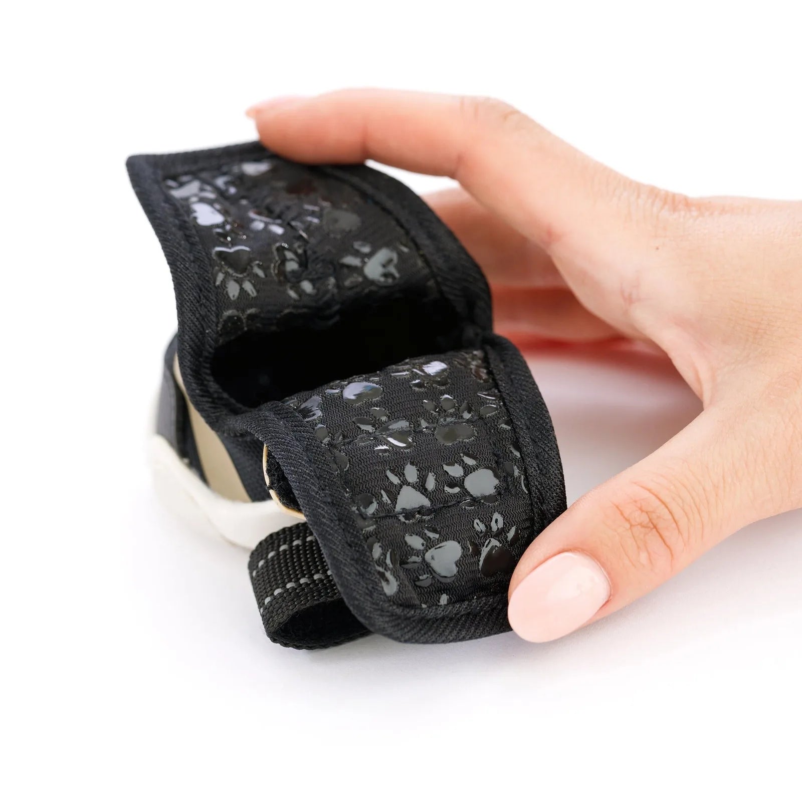 Adjustable black dog sneaker featuring paw print design, held by a hand, showcasing its opening and secure straps.