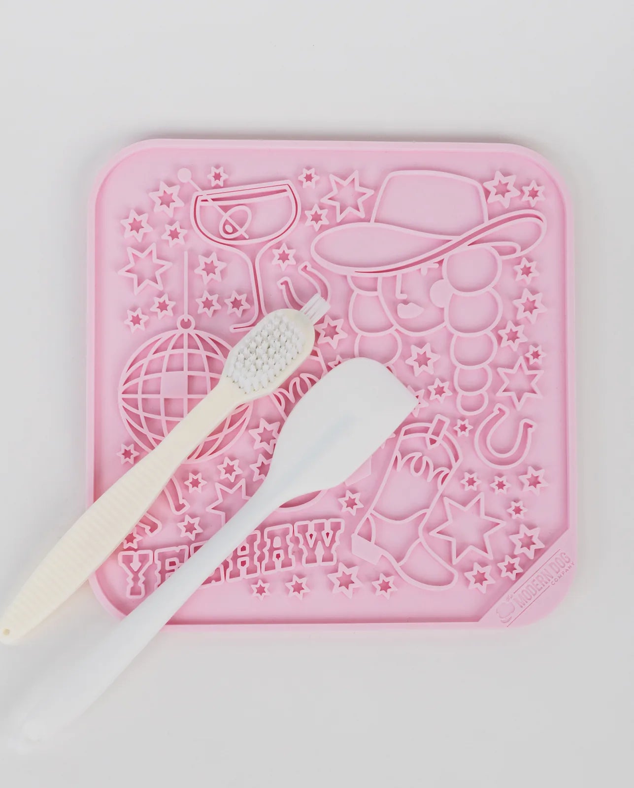 Pink silicone lick mat featuring fun designs and two accessories: a spatula and a brush for easy application and cleaning.