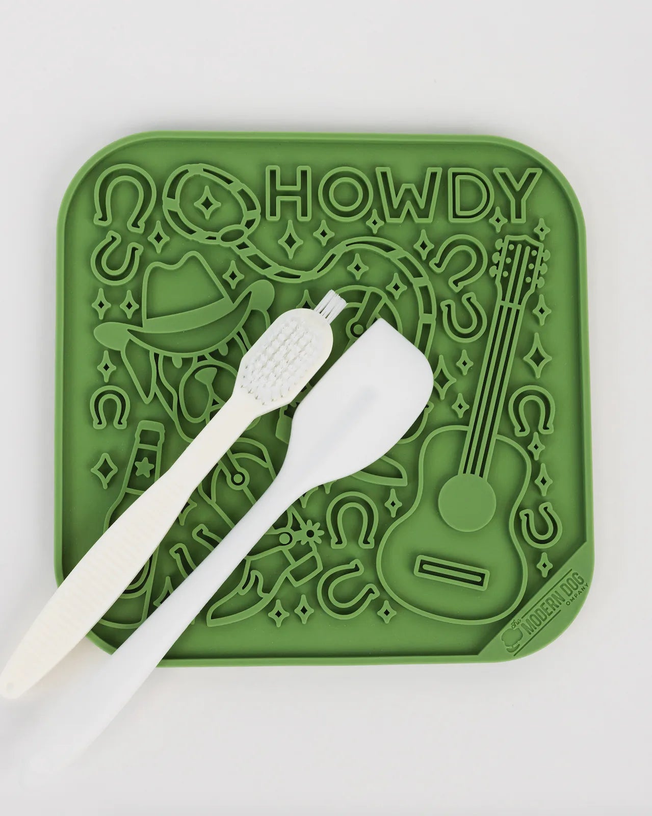 Green silicone Howdy lick mat with playful design, featuring a spatula and scrub brush for treats and cleaning.