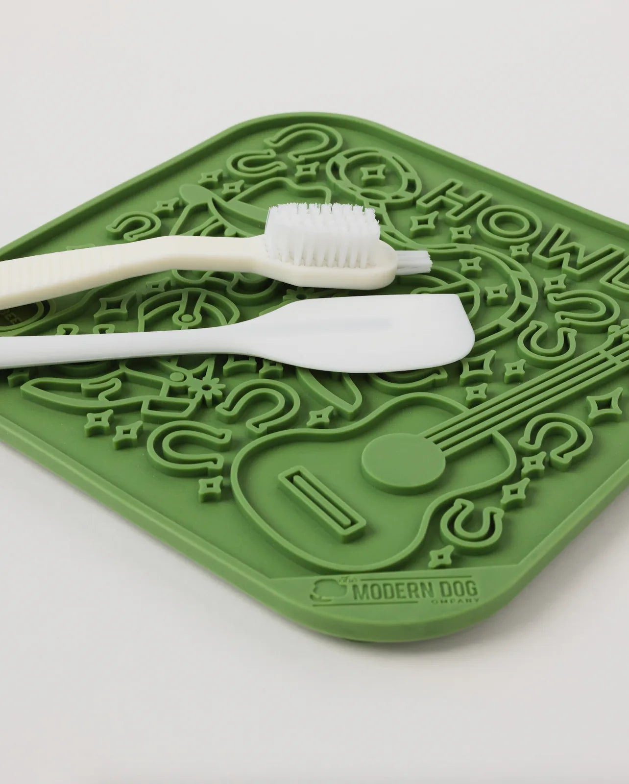 Green silicone lick mat featuring raised designs, a white spatula, and a scrub brush for easy cleaning.