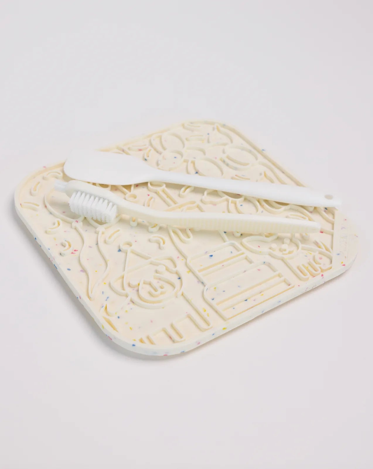 Birthday-themed lick mat in cream with colorful speckles, paired with a spatula and scrub brush for easy cleaning.
