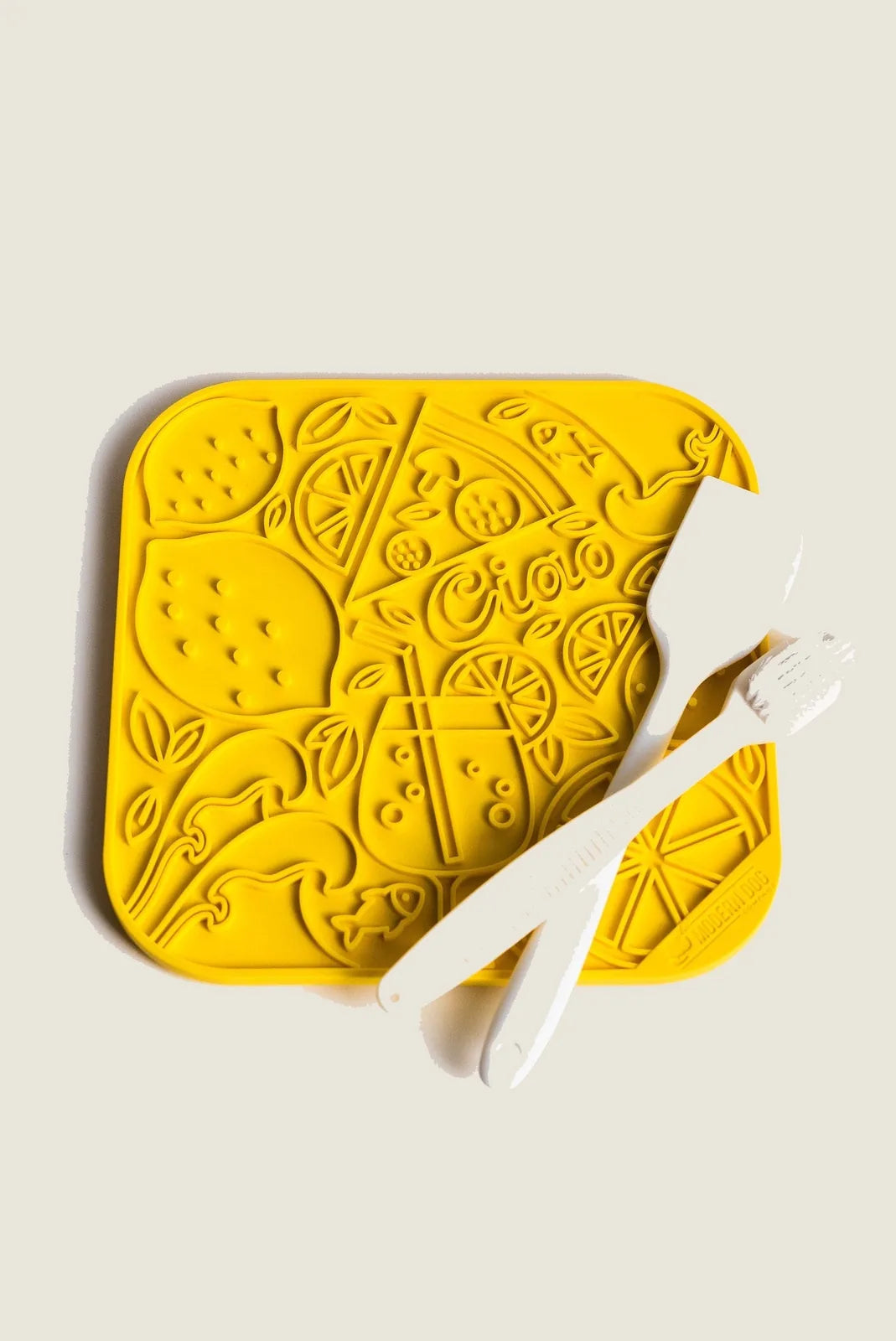 Bright yellow Limoncello Lick Mat with playful fruit designs, accompanied by two white silicone tools for easy use.