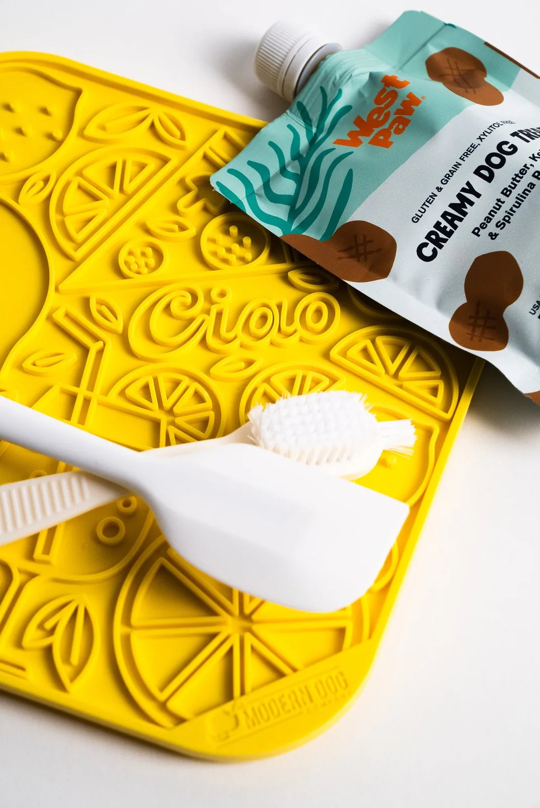 Limoncello lick mat in bright yellow silicone, featuring fun citrus designs, with a white spatula and dog treat pouch.