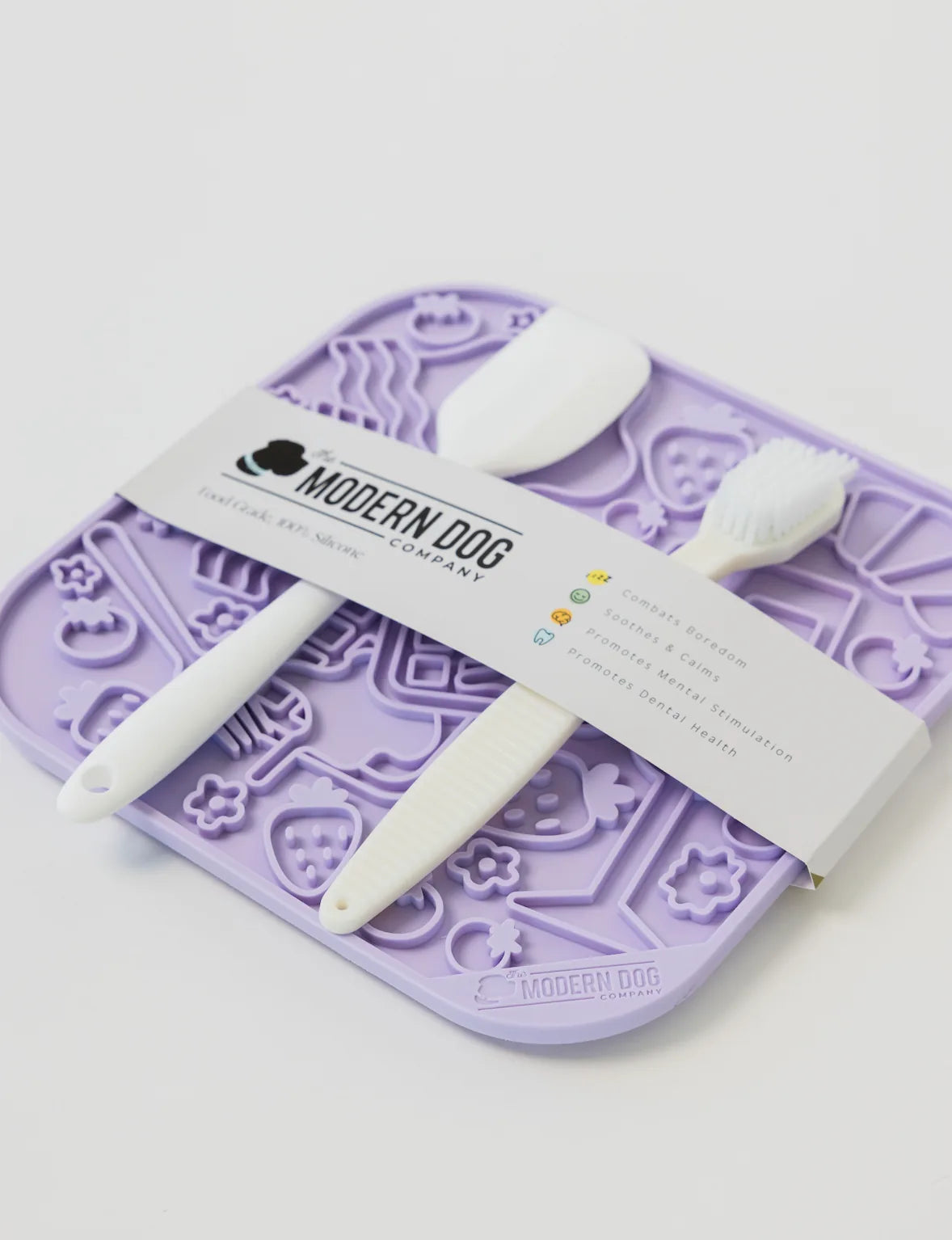 Purple silicone lick mat with textured designs, accompanied by a spatula and scrub brush for spreading and cleaning treats.