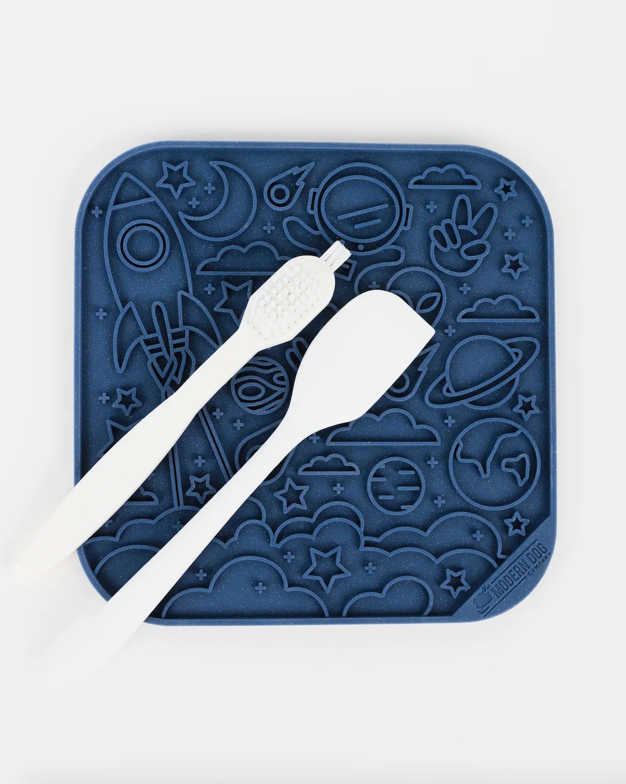 Navy silicone lick mat with space-themed designs, accompanied by a spatula and scrub brush for dogs.