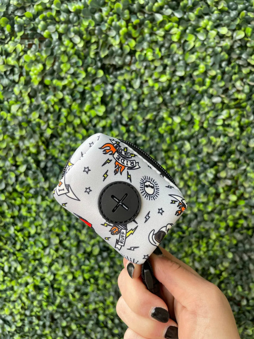 White poop bag holder featuring playful dog-themed graphics, crafted from lightweight neoprene, held against a green backd...
