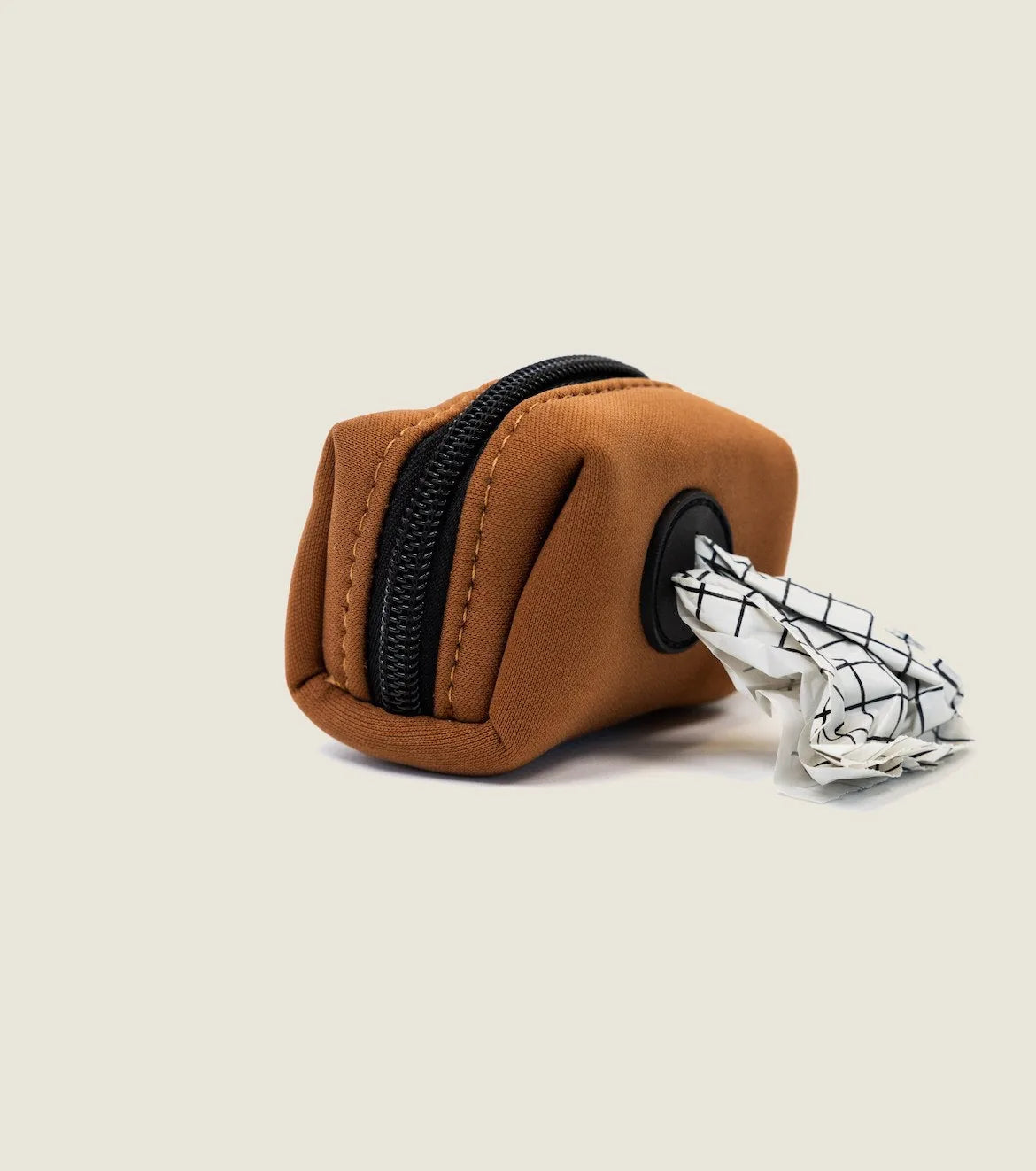 Compact brown neoprene dog waste bag holder with a black zipper, showcasing a rolled-up bag emerging from the side.