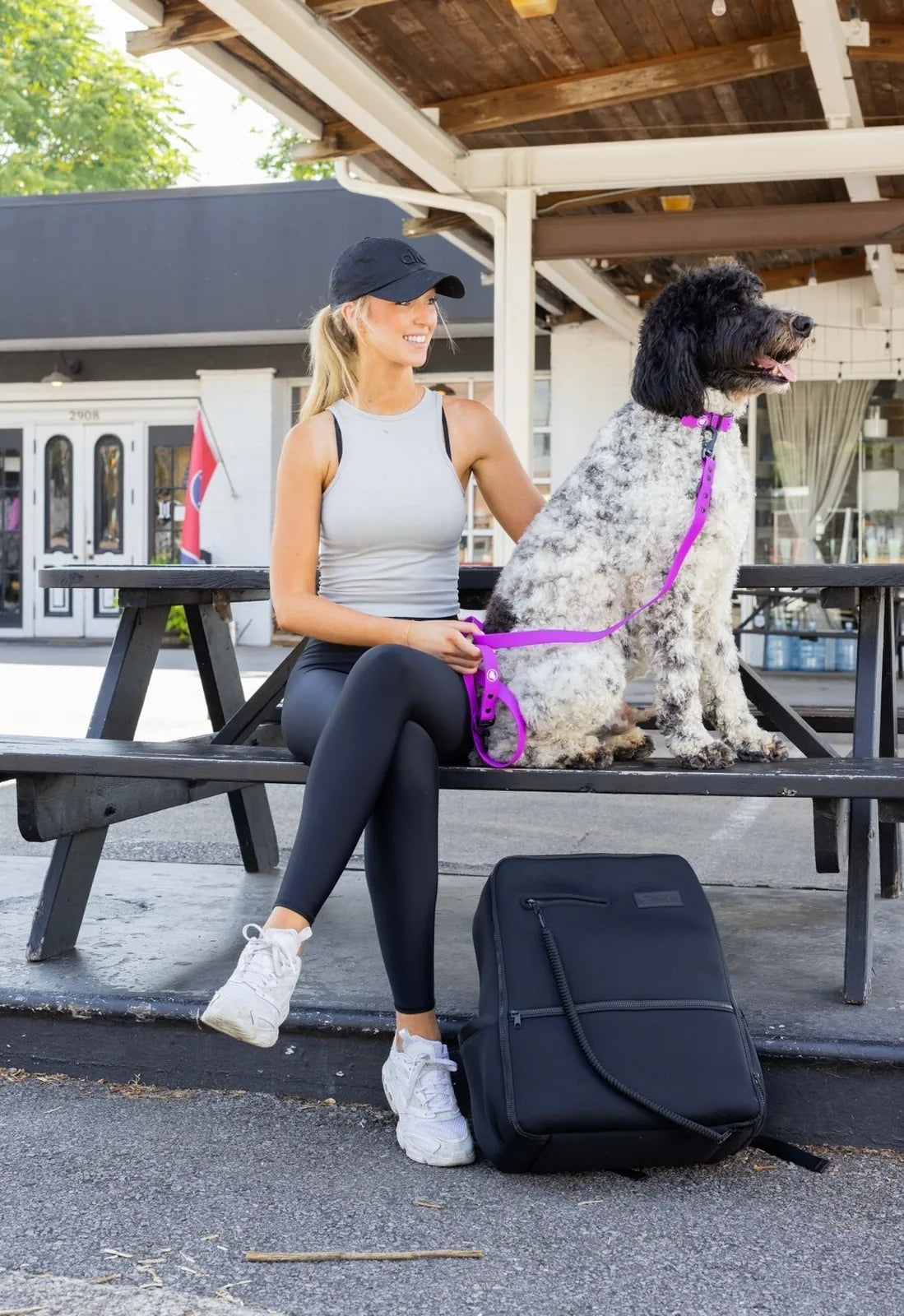 A woman in athletic wear sits on a bench with a fluffy dog, holding a bright fuchsia adjustable dog leash.