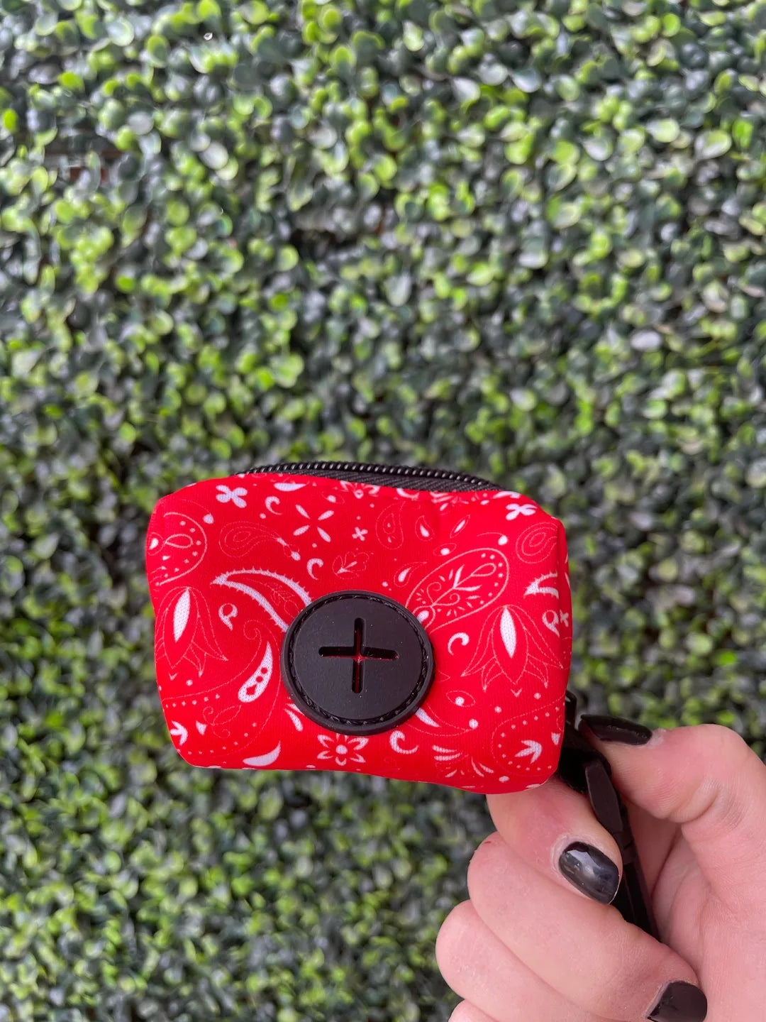 Red neoprene dog waste bag holder with paisley pattern, featuring a clip for easy attachment to leashes.
