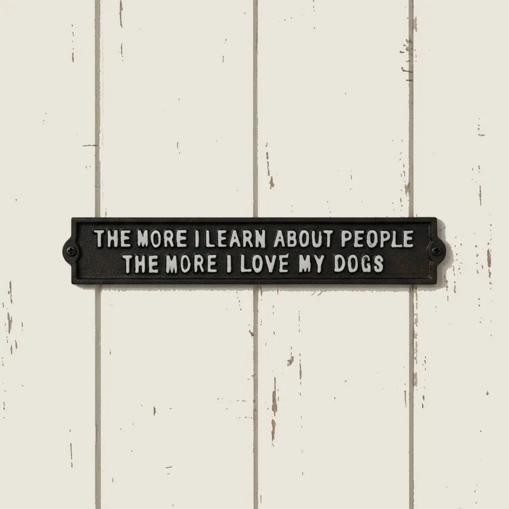 Cast iron wall plaque featuring the phrase, "The More I Learn About People, The More I Love My Dogs," on a light wood back...