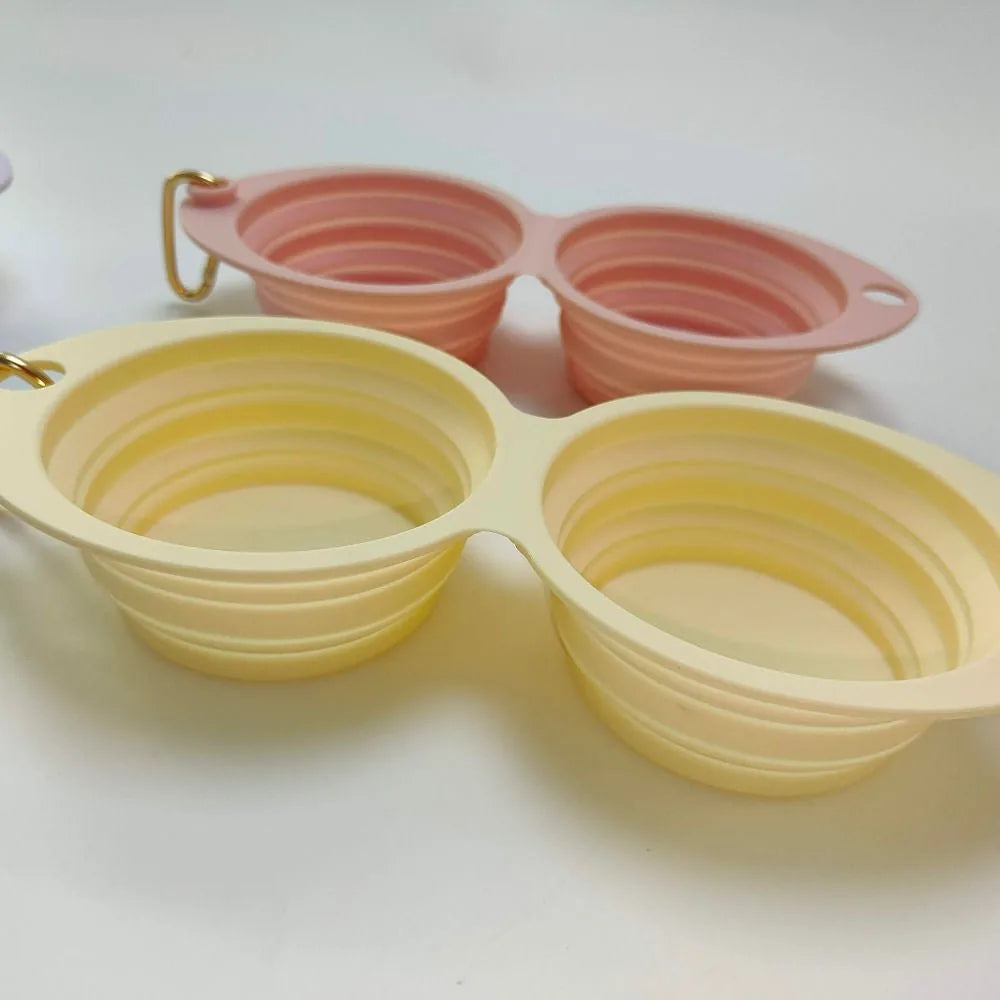 Collapsible double pet bowl in soft pink and yellow silicone, perfect for travel with compartments for food and water.