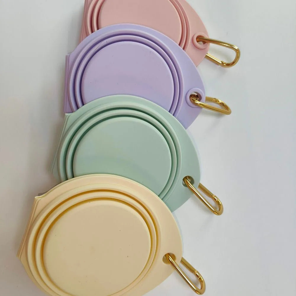 Collapsible double pet bowls in Banana, Lilac, Pink, and Mint Green, featuring gold clips for easy attachment.