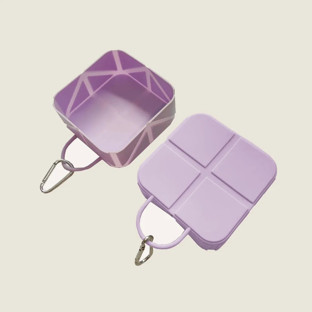Compact foldable dog bowl in lilac with a carabiner, featuring a square design with a divider for food and water.