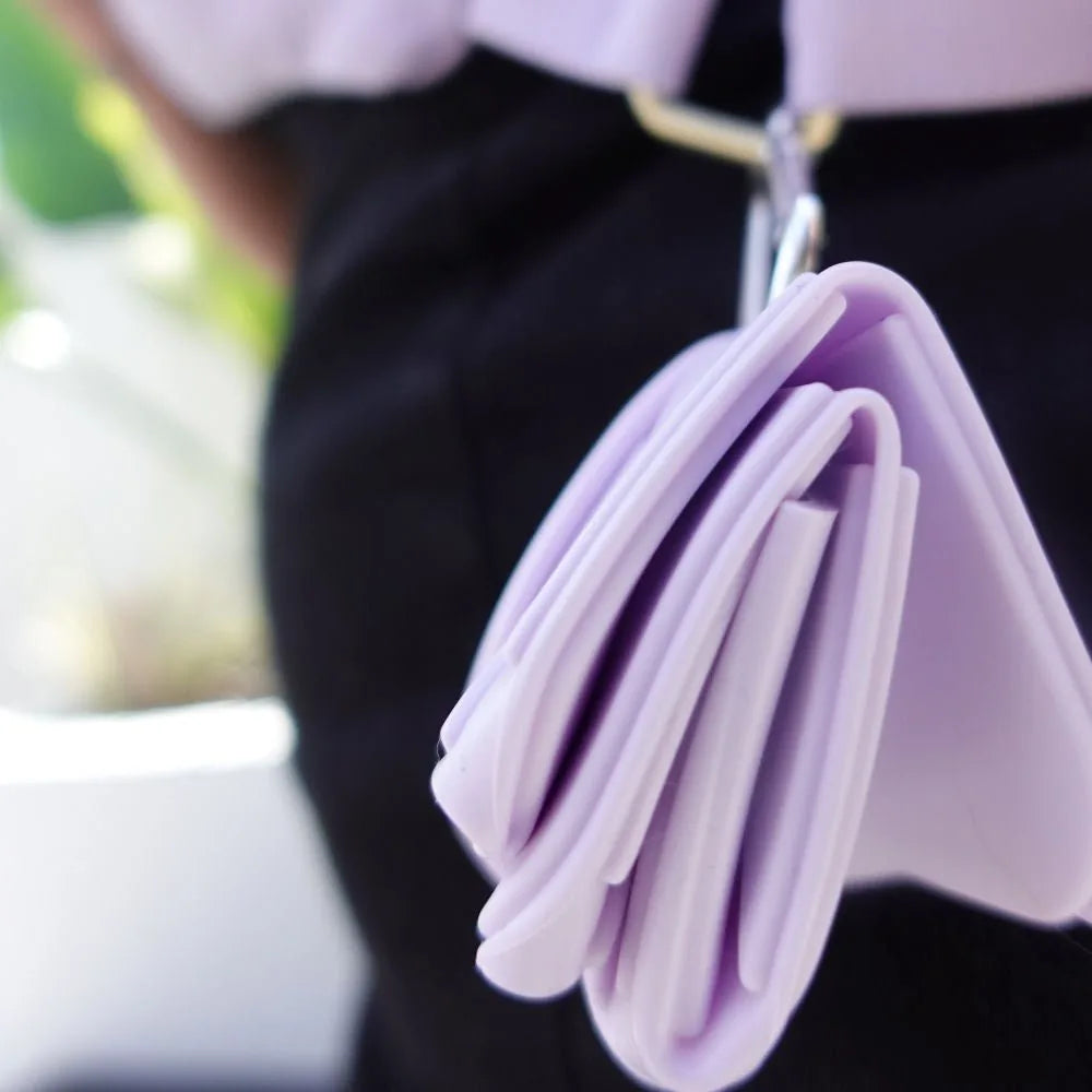 Lilac foldable pet food and water bowl hanging from a belt, showcasing its compact design for travel.