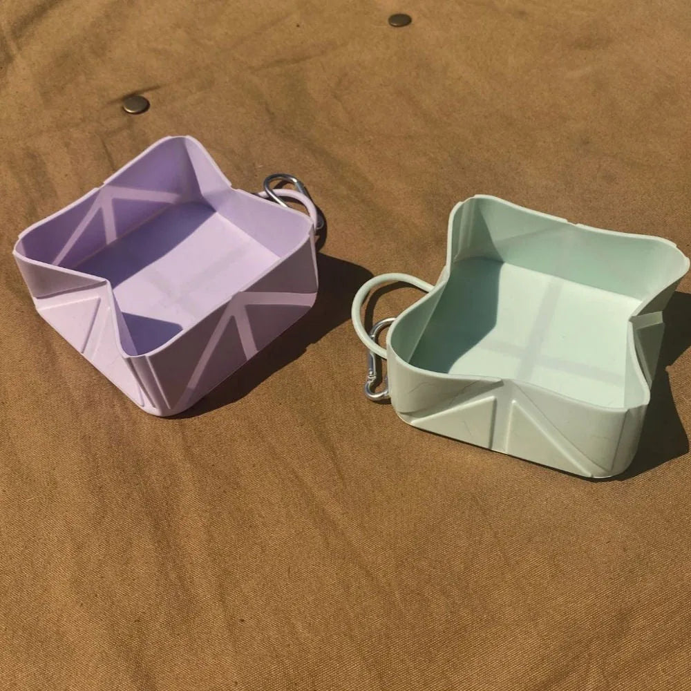 Compact foldable dog bowls in lilac and mint green displayed on a brown surface, featuring a practical design for travel.