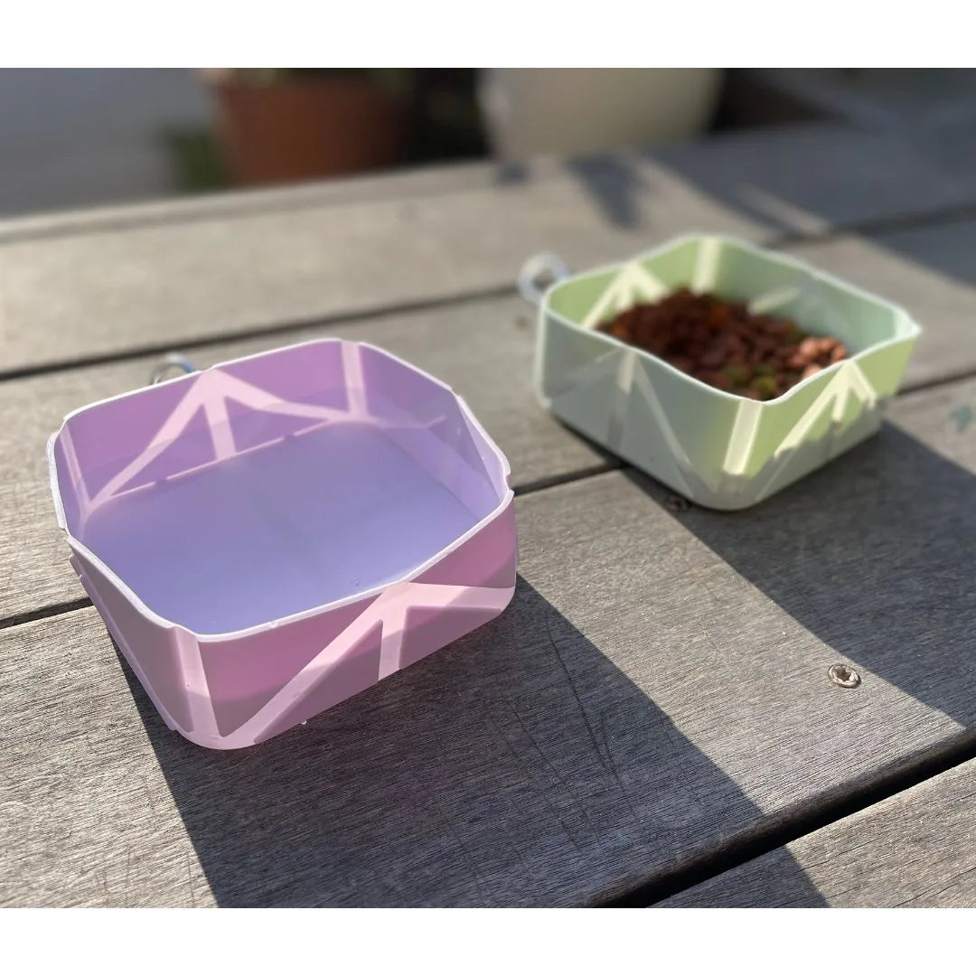 Compact foldable pet bowls in lilac and mint green with dog food, positioned on a wooden surface for outdoor use.