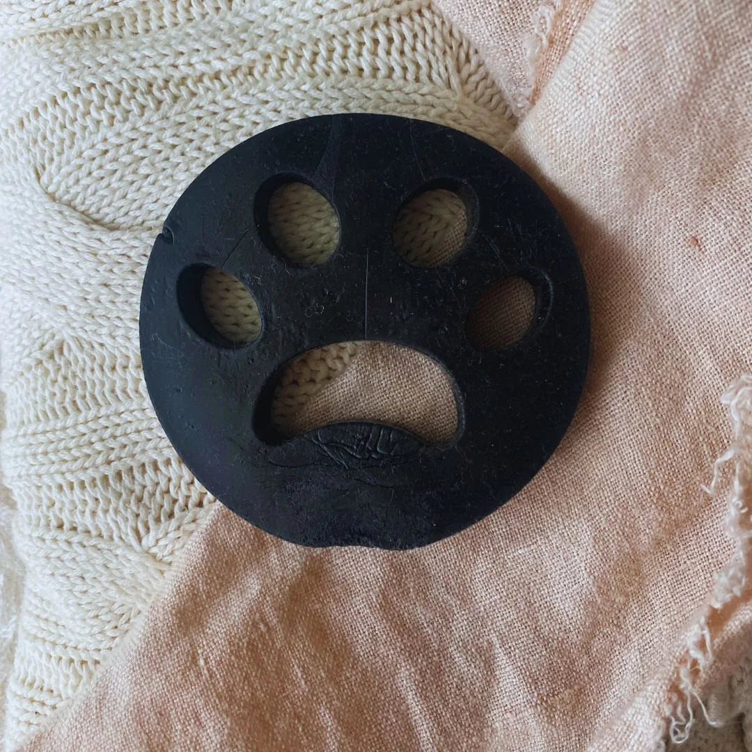 Black paw-shaped lint remover resting on a soft, neutral fabric background, ideal for pet hair management.