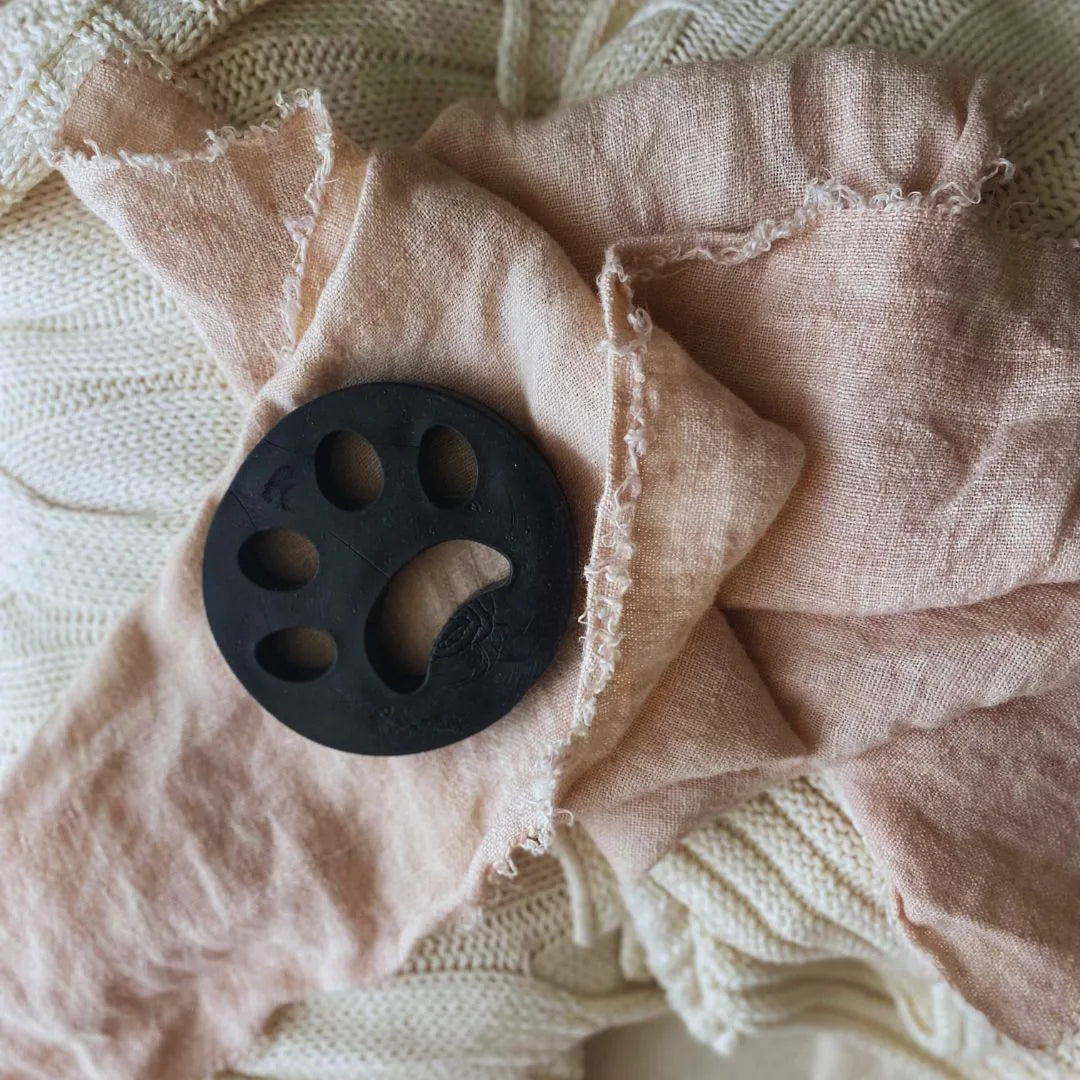 Black reusable lint remover lies on soft, wrinkled peach and cream fabrics, ideal for pet hair removal in laundry.