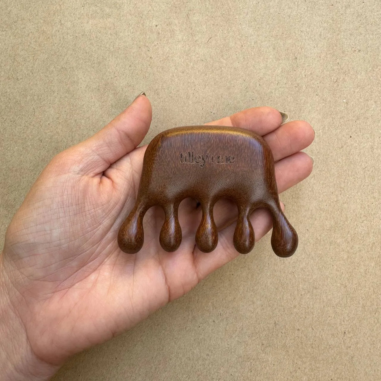Sandalwood pet massage tool held in hand, featuring a smooth brown finish and five rounded prongs for grooming.