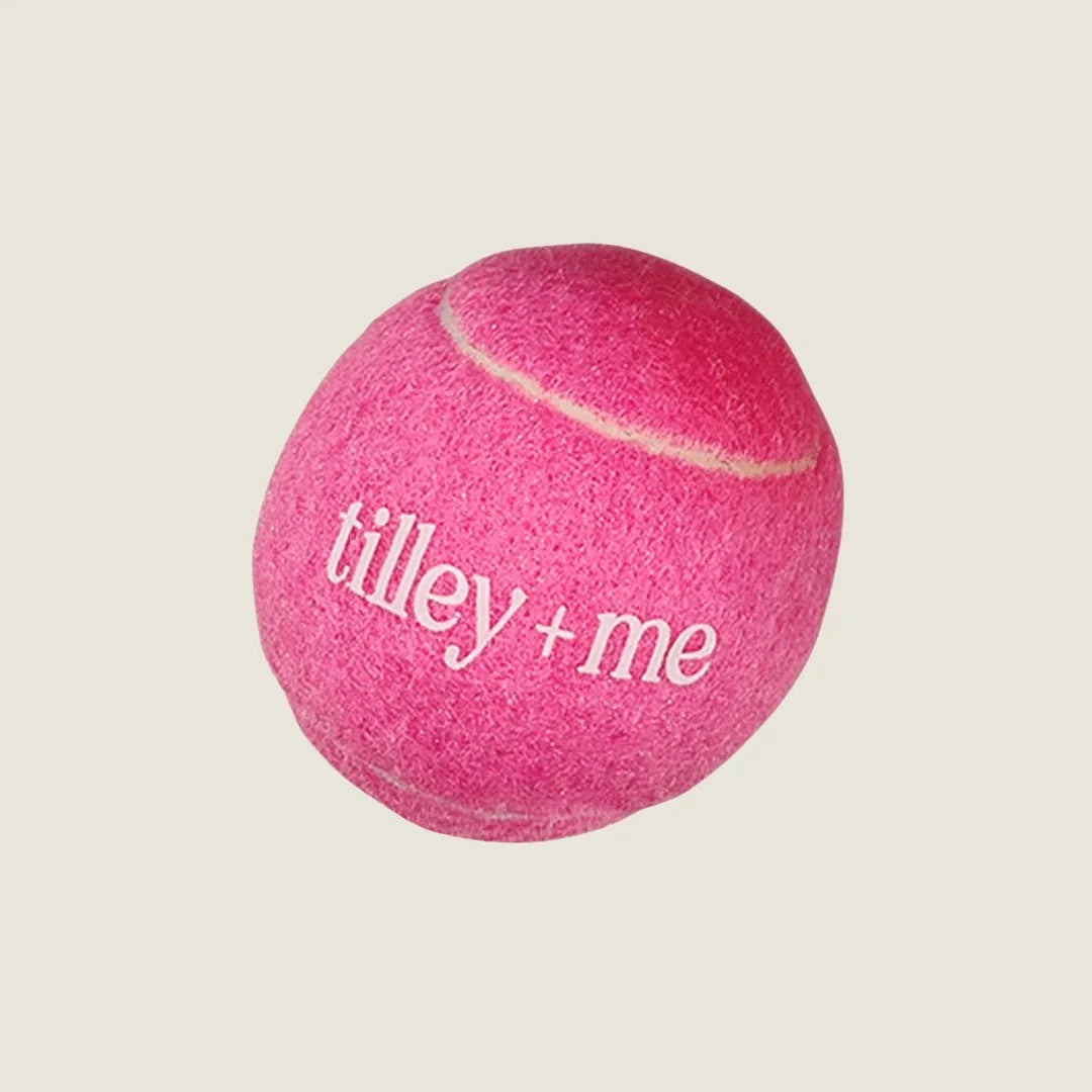 Bright Barbie Pink tennis ball with "tilley + me" logo, perfect for dogs to fetch and play indoors or outdoors.